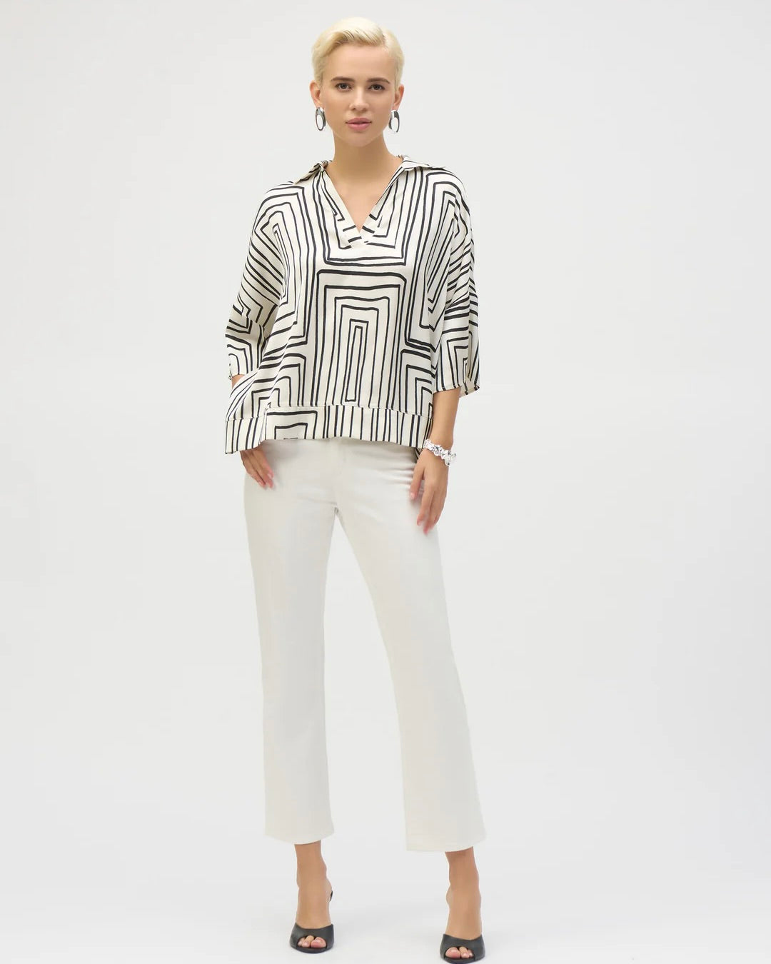 joseph ribkoff geometric boxy top on model in white jeans and black heels standing in front of white wall