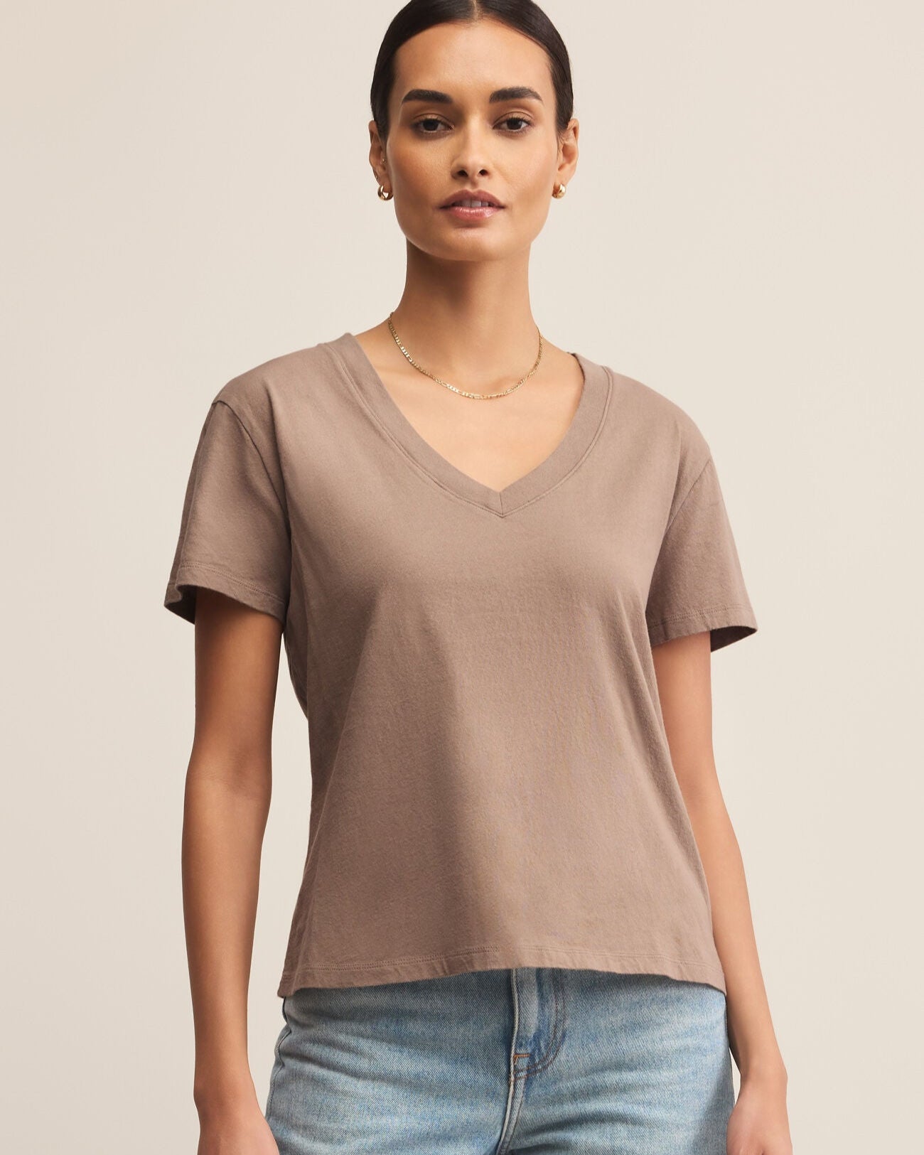 Woman wearing a brown V-neck t-shirt and light blue jeans on a beige background