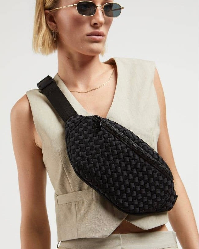 Model wearing Sol & Selene Aim High Woven Neoprene belt bag in black wearing sunglasses on a white background