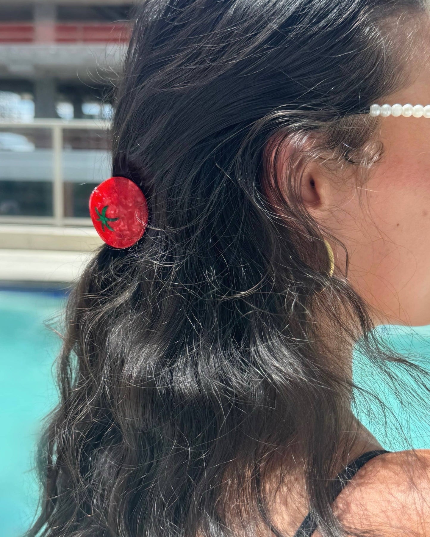 Close-up of a person's hair with a tomato clip in front of a pool and building in the background