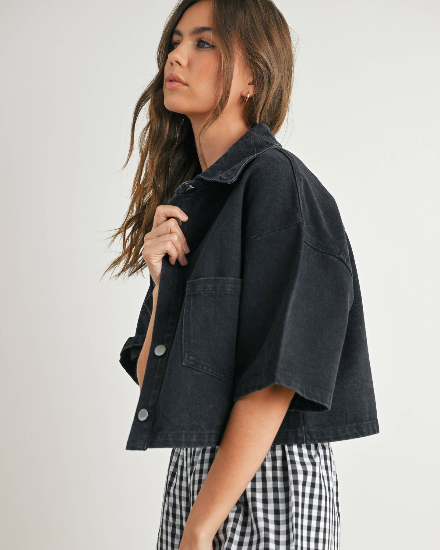 Woman wearing a black denim jacket and checkered shorts on a white background