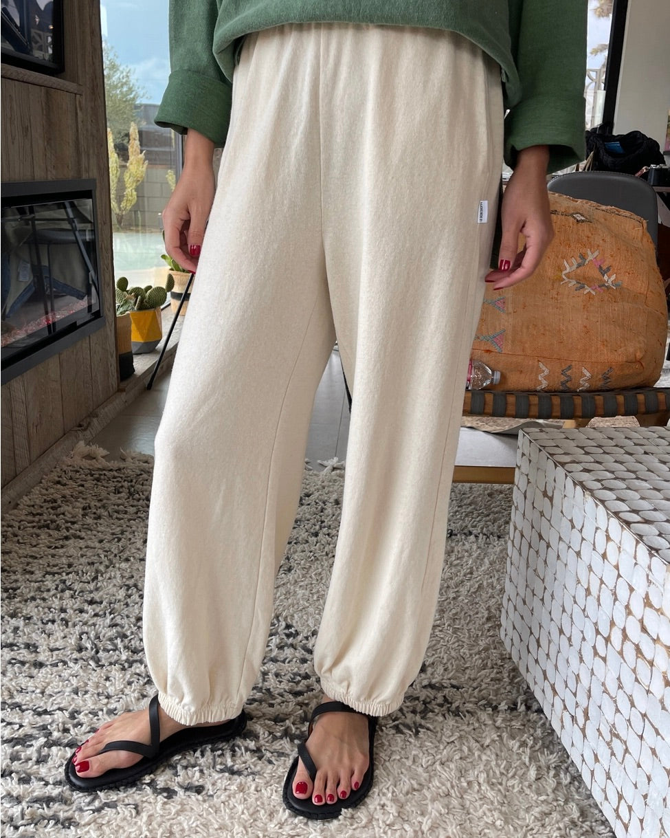 Front view of the Le Bon Shoppe balloon pant in naturel on a model standing in a living room with boho decor