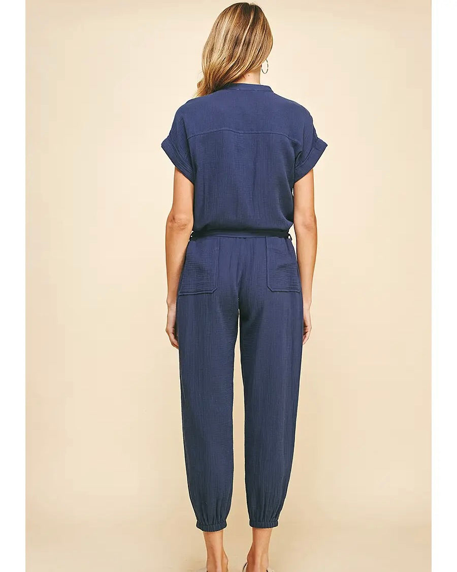 Model wearing PINCH button front jumpsuit in Navy on a brown background