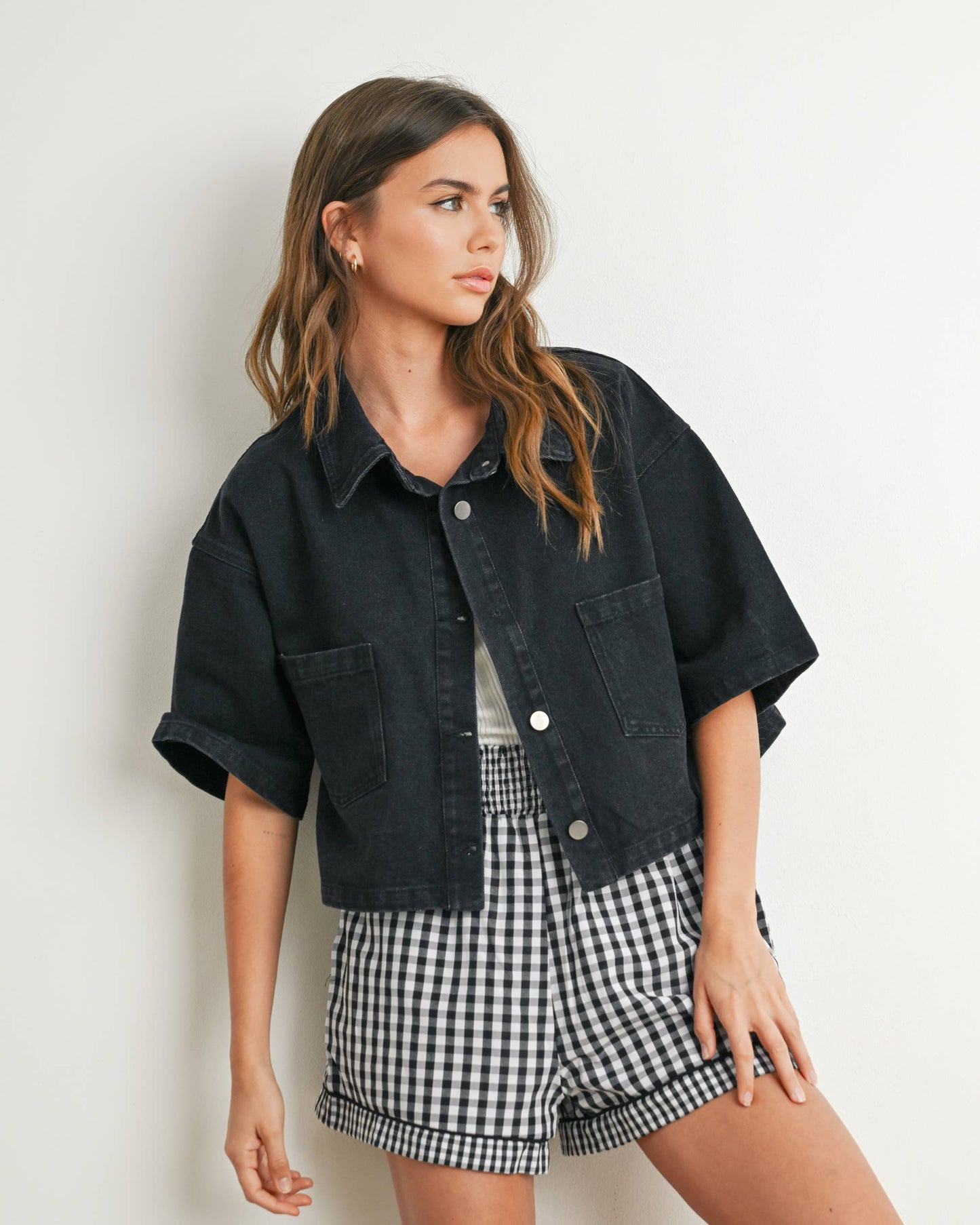 Woman wearing a black denim jacket and checkered shorts against a white background