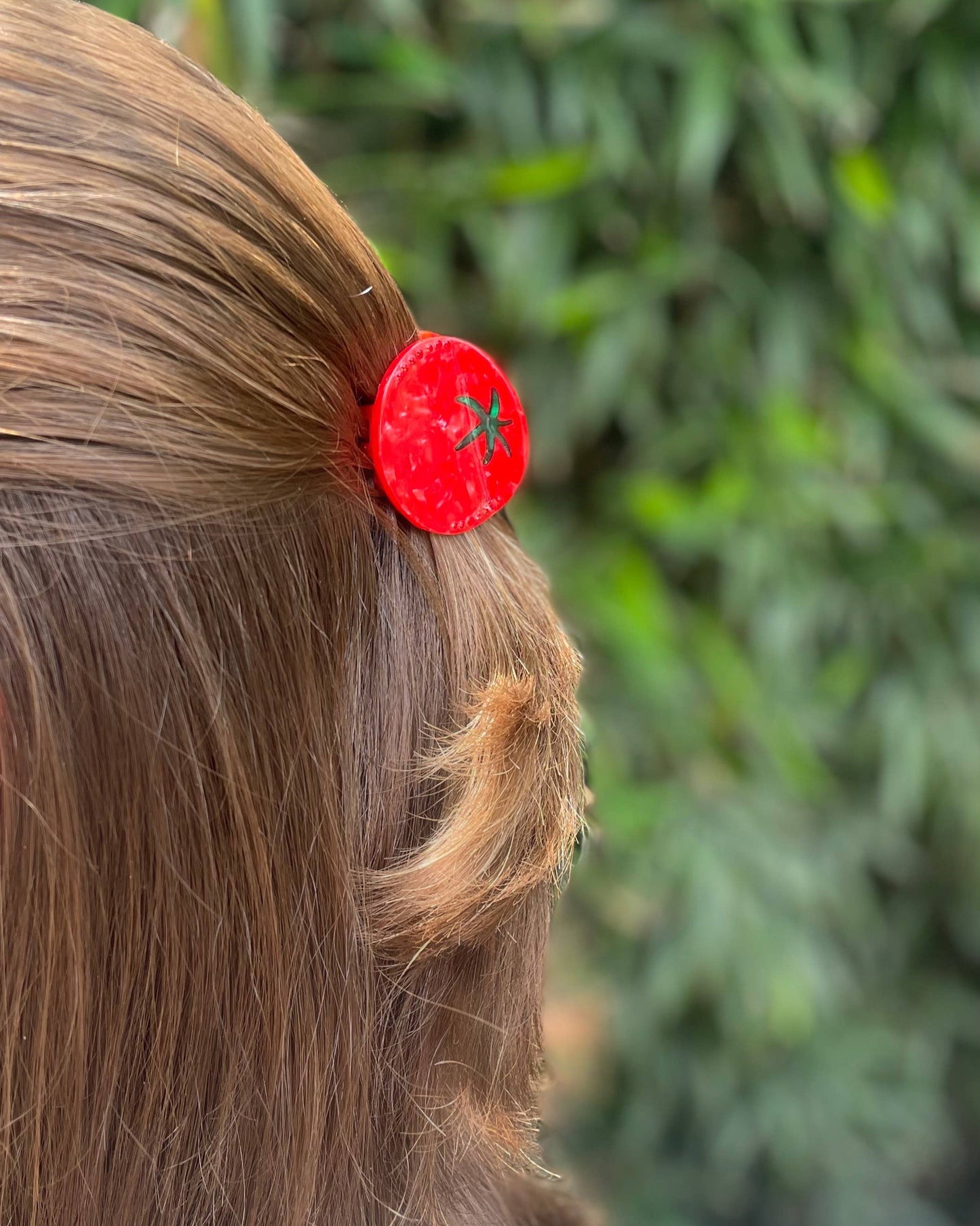Tomato hair clip with a green leaf design on a person's hair against a blurred green background
