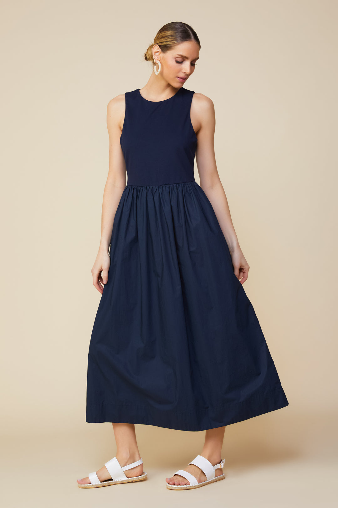 Model wearing Skies are Blue Alice High Neck Midi Dress in Navy wearing white sandals on a beige background