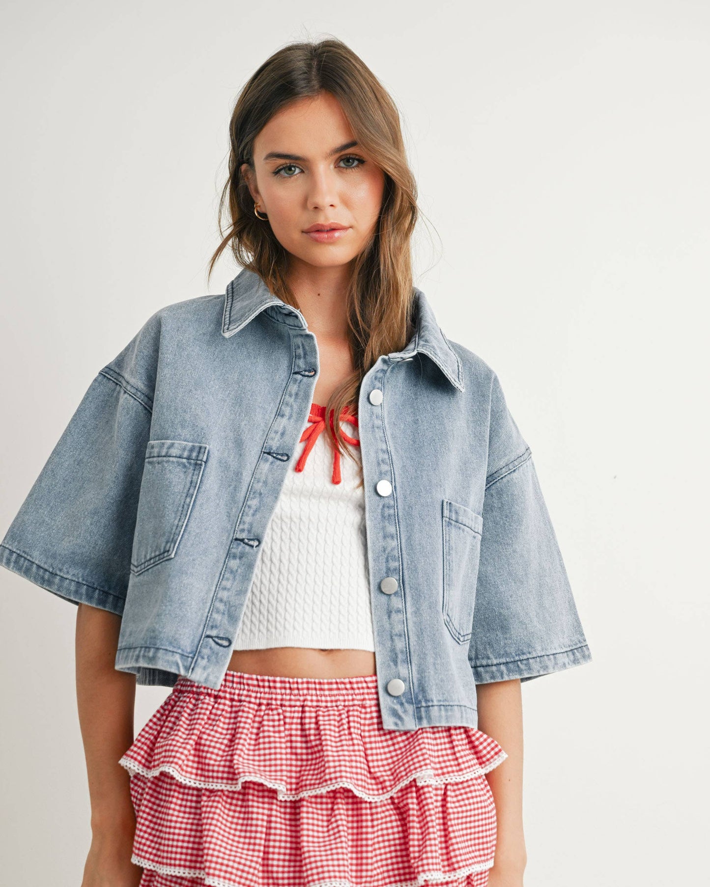 Woman wearing a denim jacket, white top, and red checkered skirt on a plain background