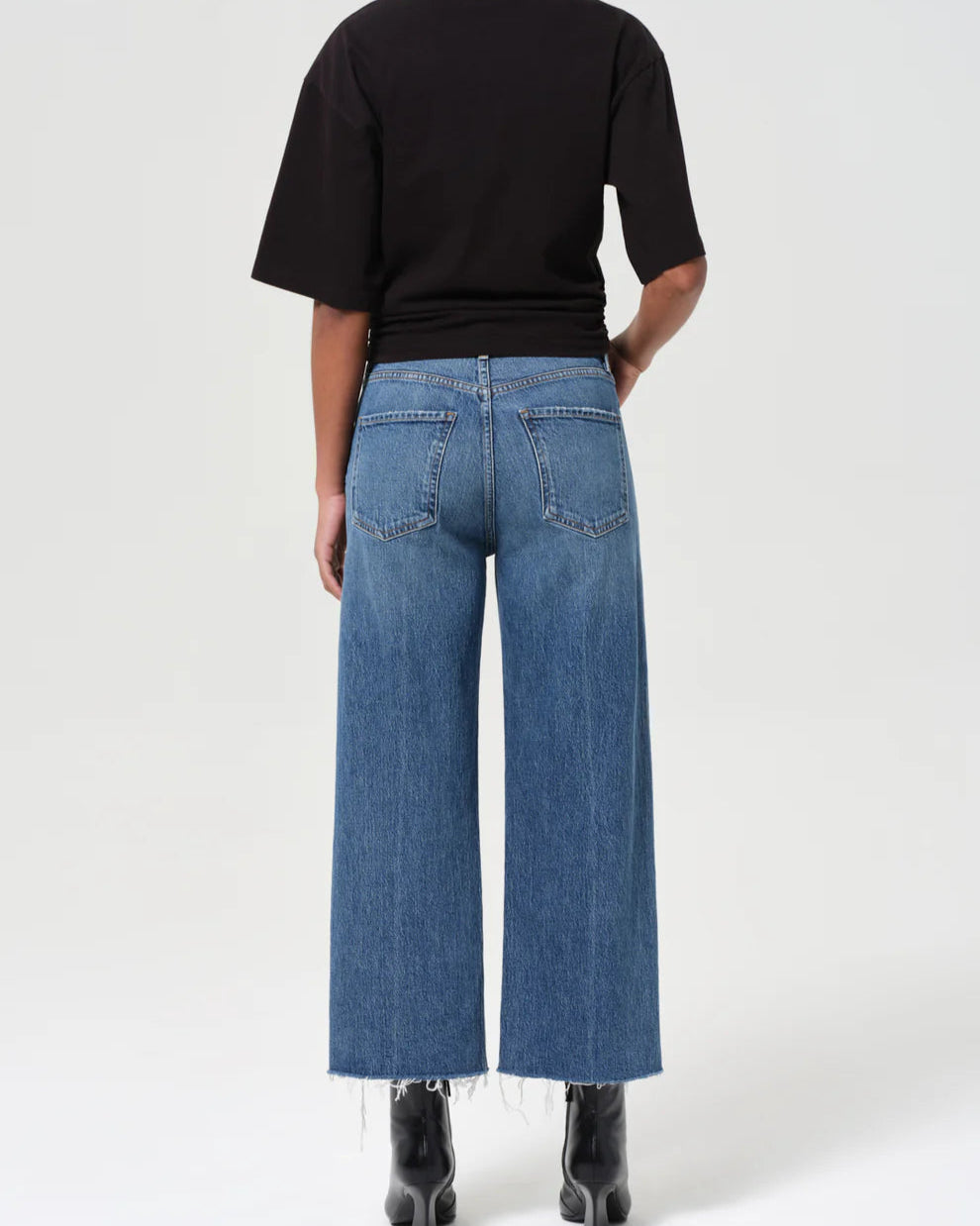 Person wearing blue jeans and a black top on a white background