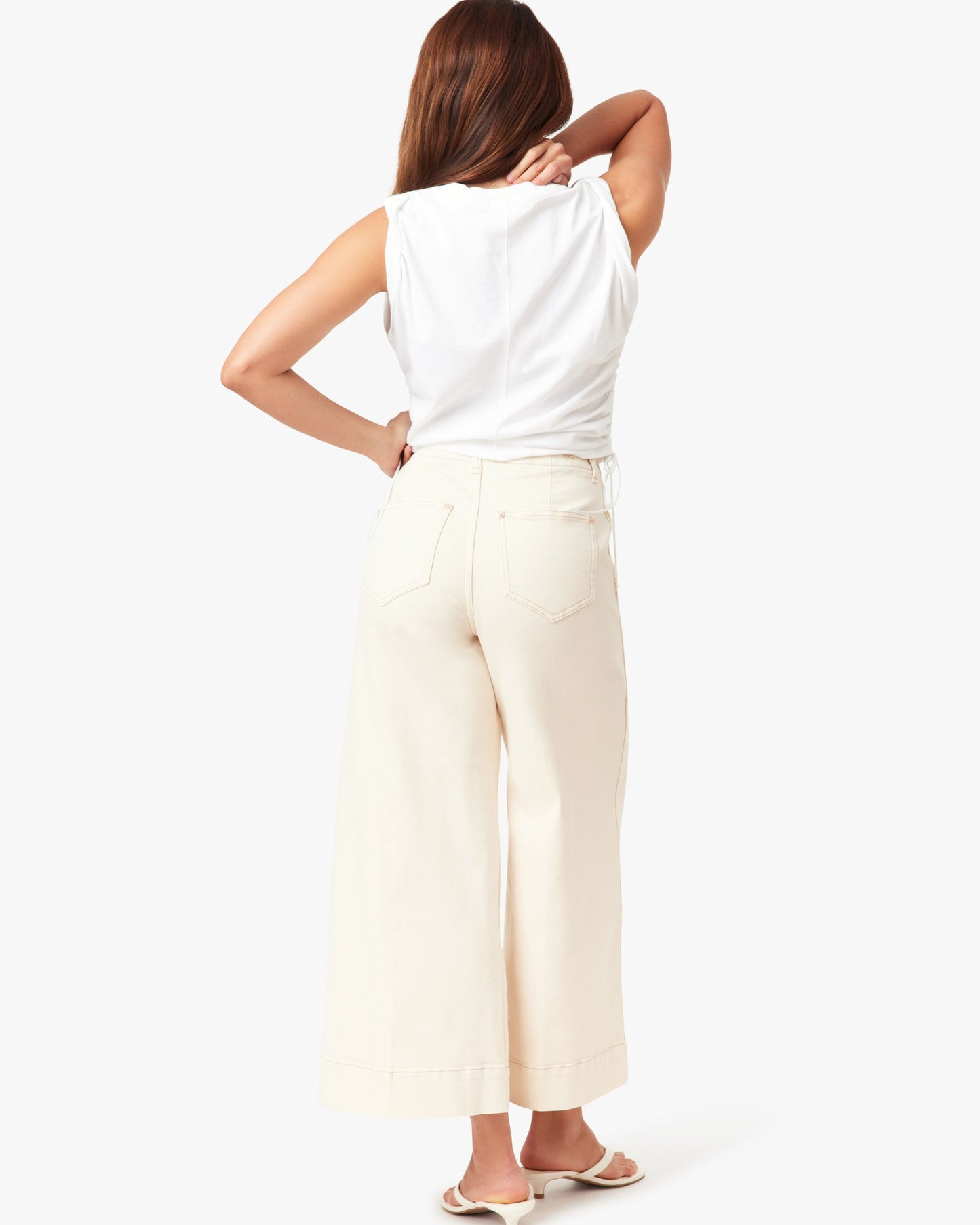 Woman wearing a white sleeveless top and beige wide-leg pants on a white background