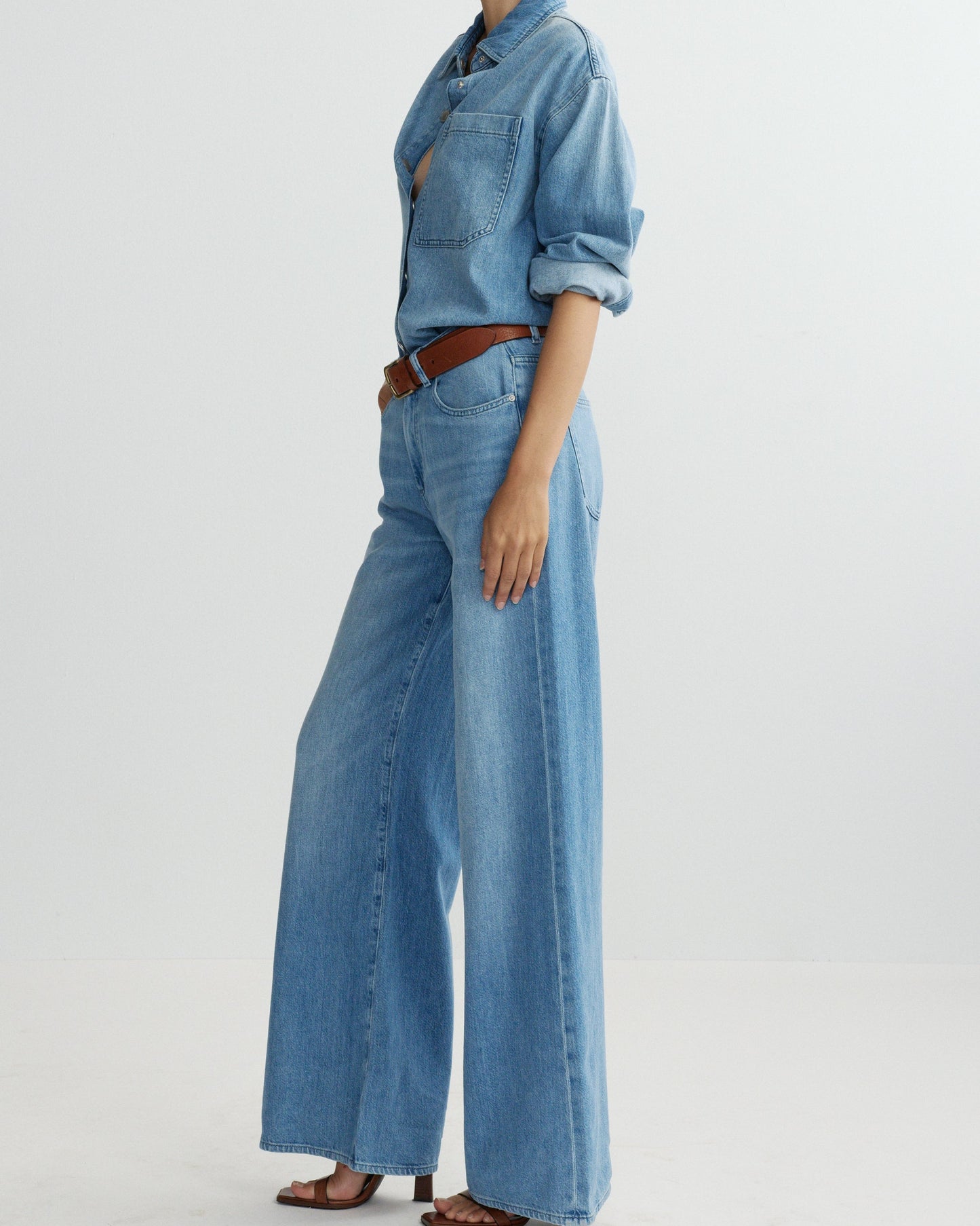Person wearing a blue denim outfit with wide-leg jeans on a light gray background