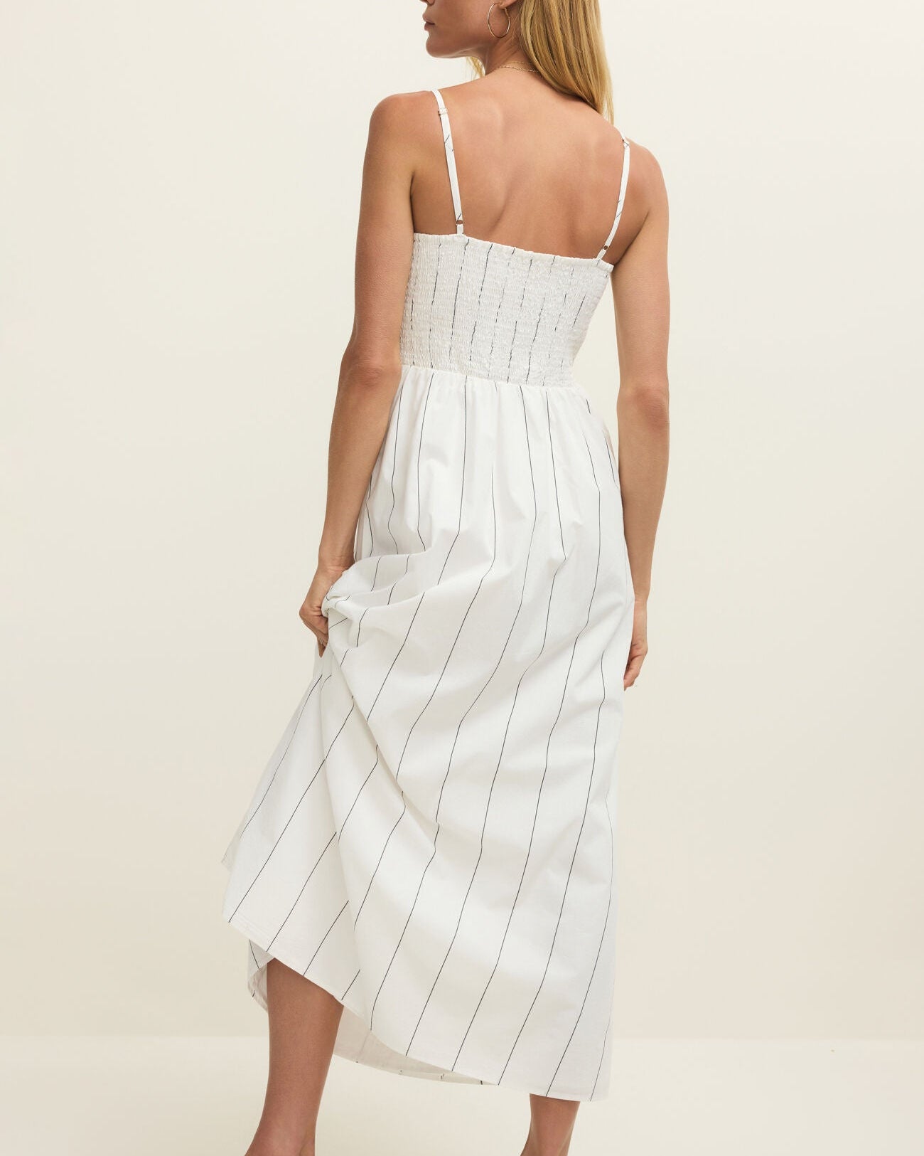 Woman wearing a white dress with thin black stripes against a plain background