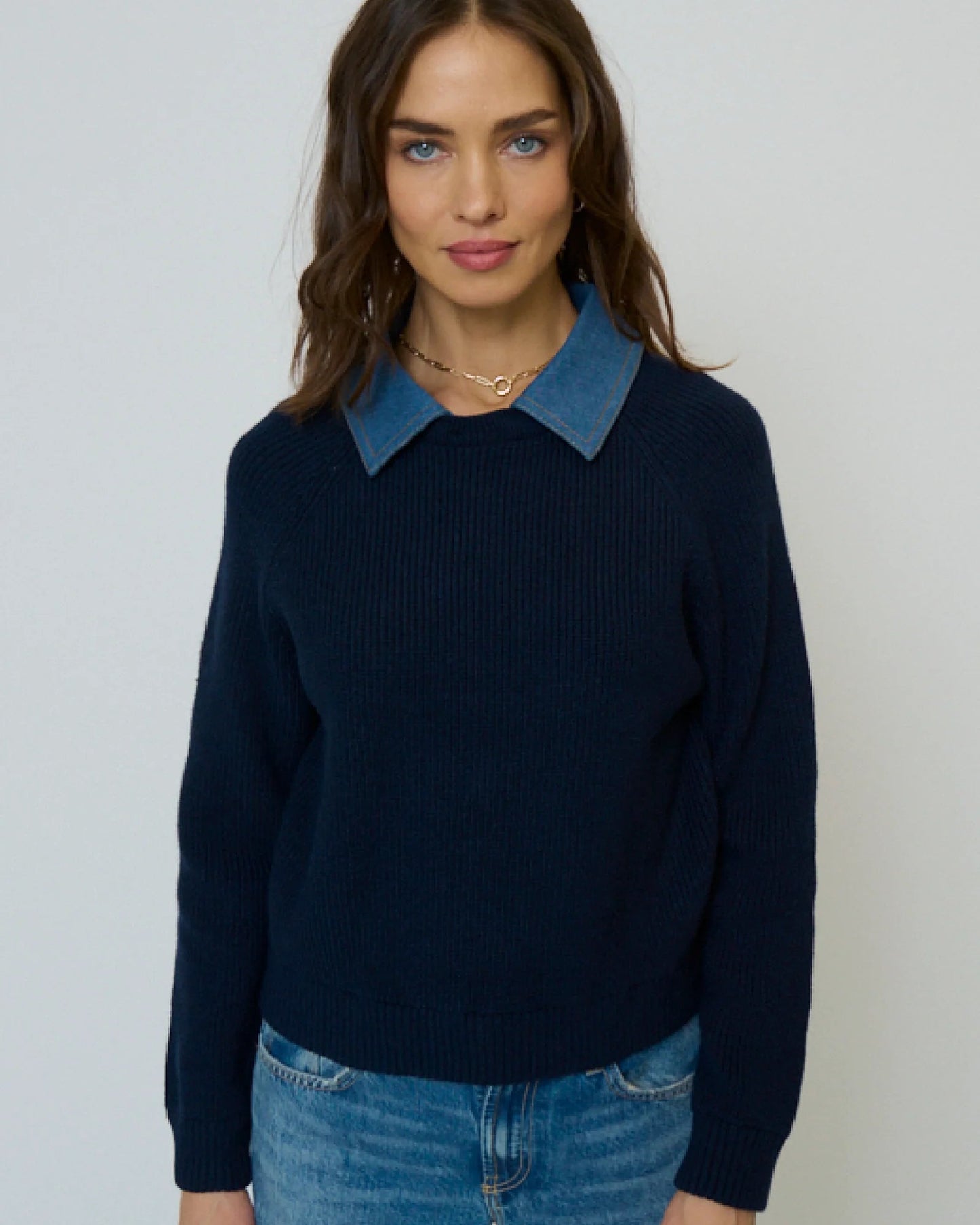 Woman wearing a navy sweater with a blue denim collar against a plain background