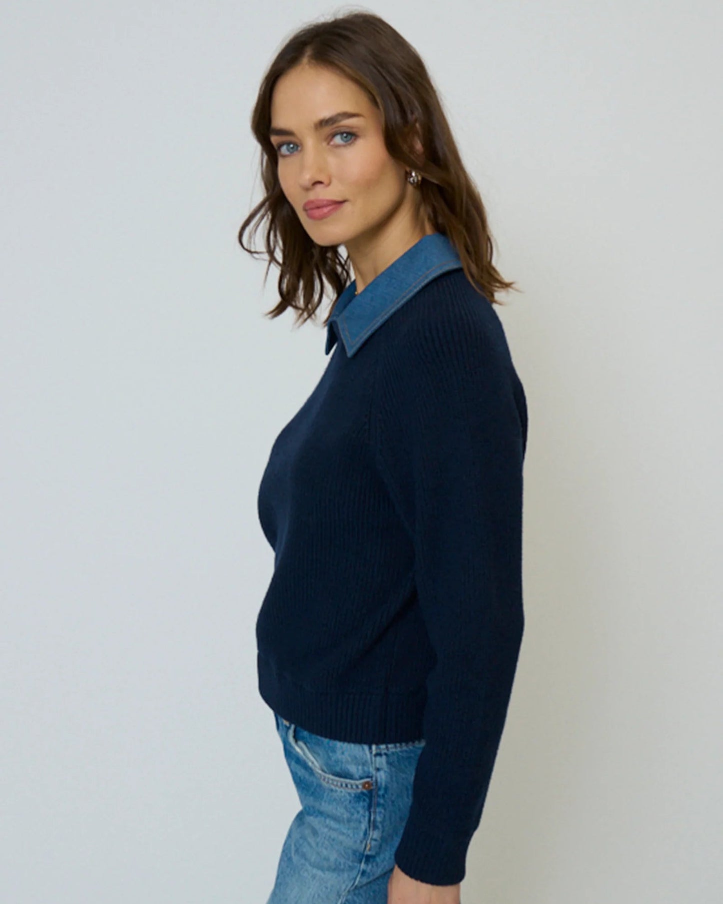 Woman wearing a navy sweater with a blue denim collar against a white background