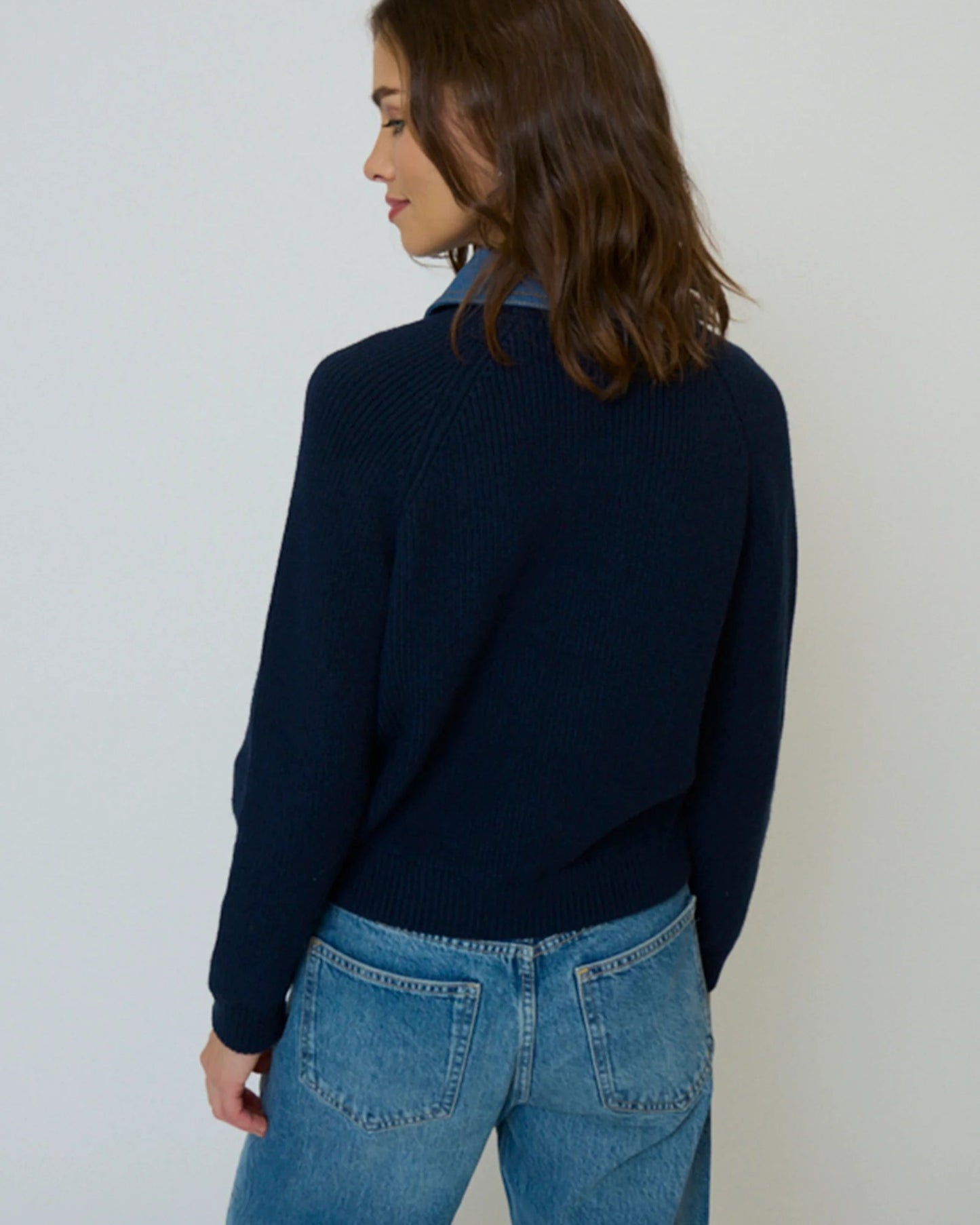 Person wearing a navy sweater and blue jeans against a white background