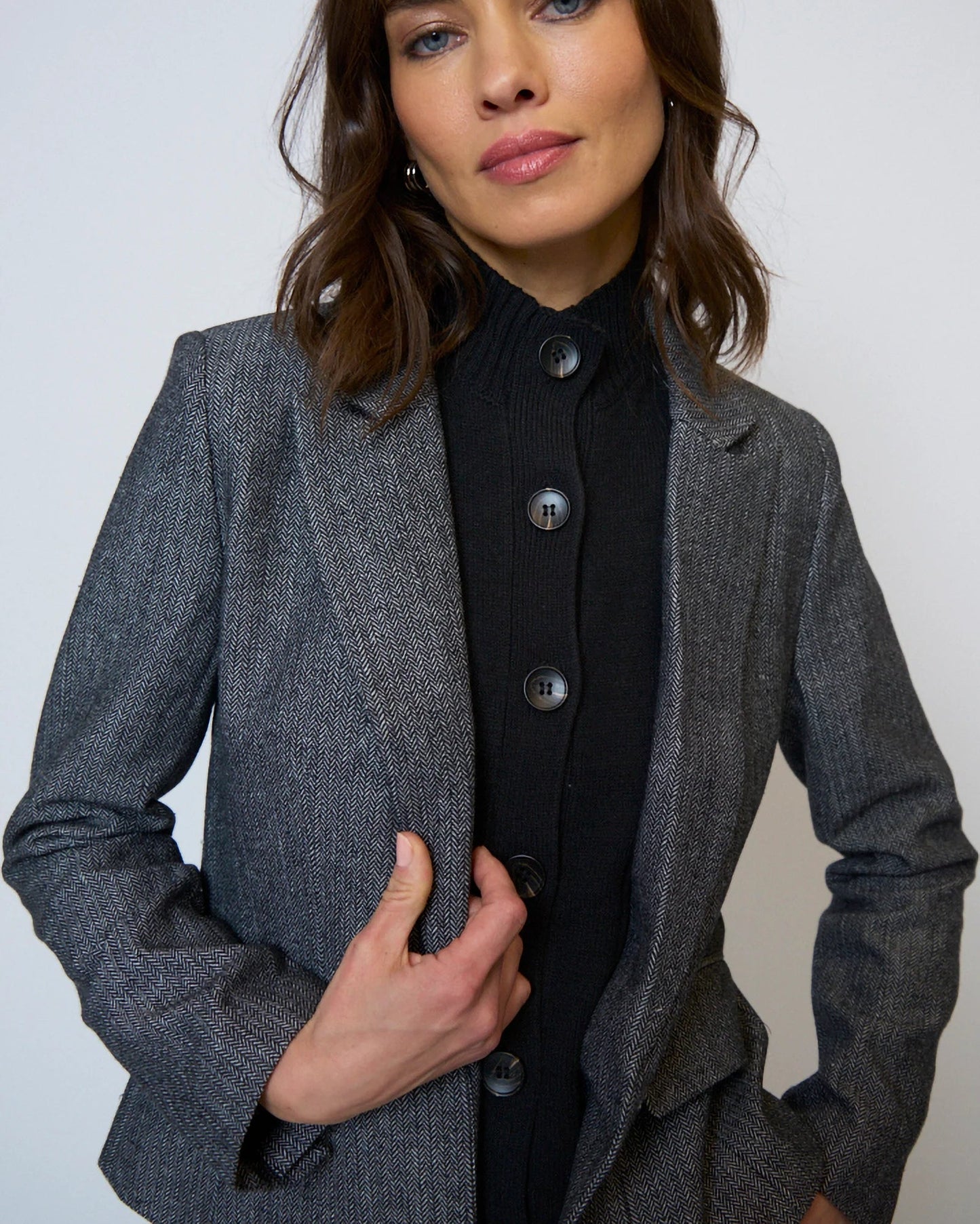 Woman wearing a gray blazer over a black outfit against a plain background