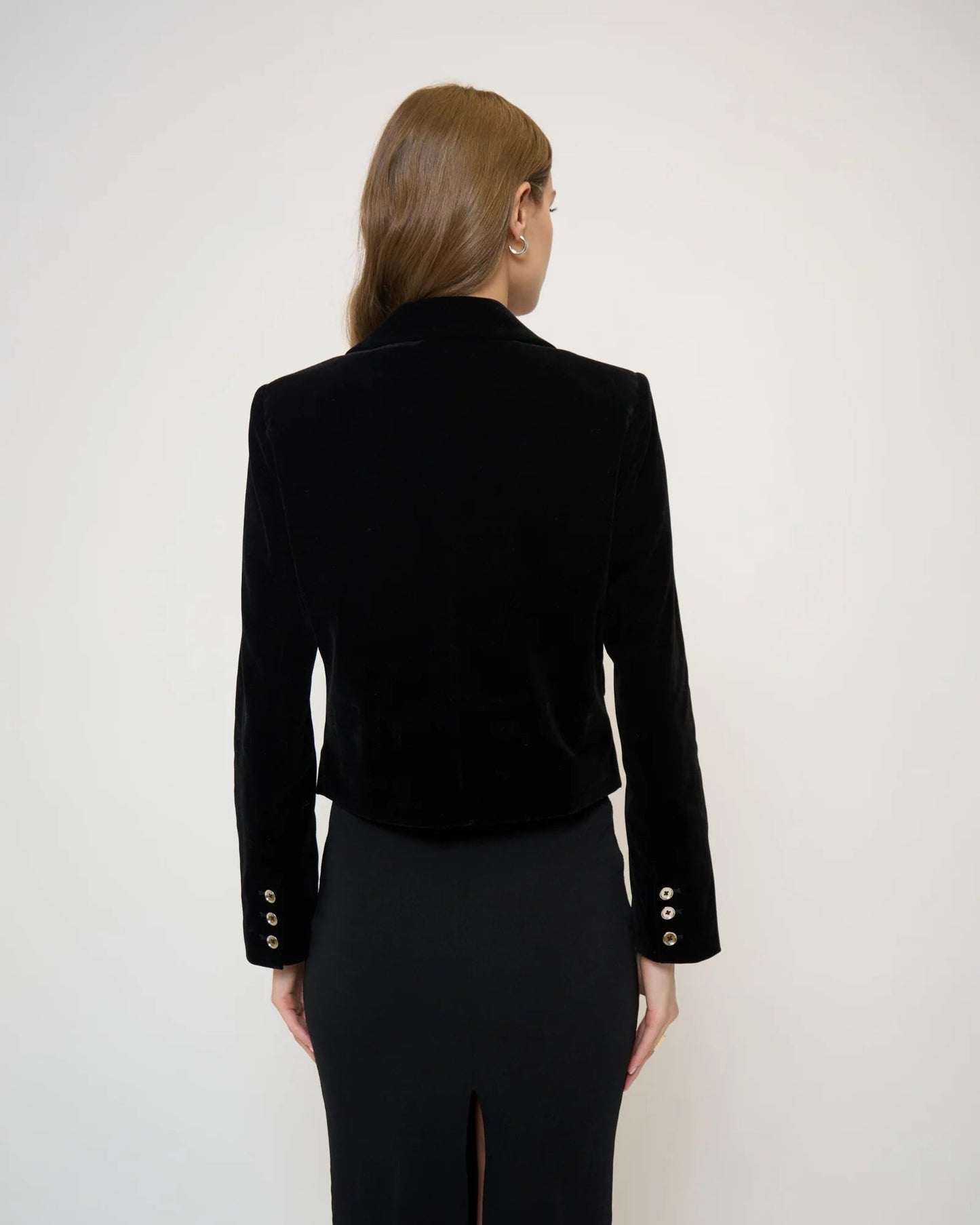 Back view of a model wearing a velvet jacket and black skirt in front of a white background