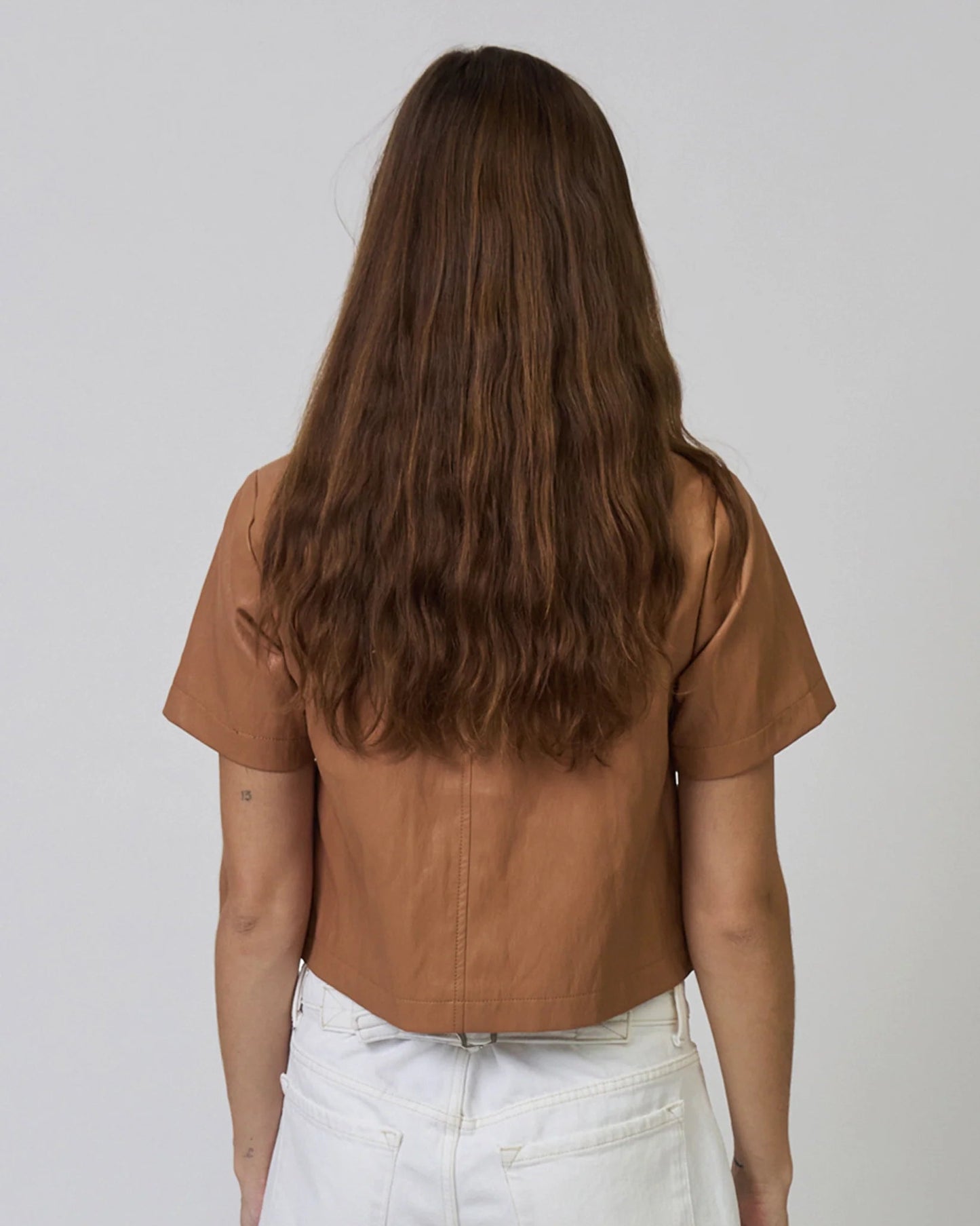 Person wearing a brown leather top and white pants against a plain background