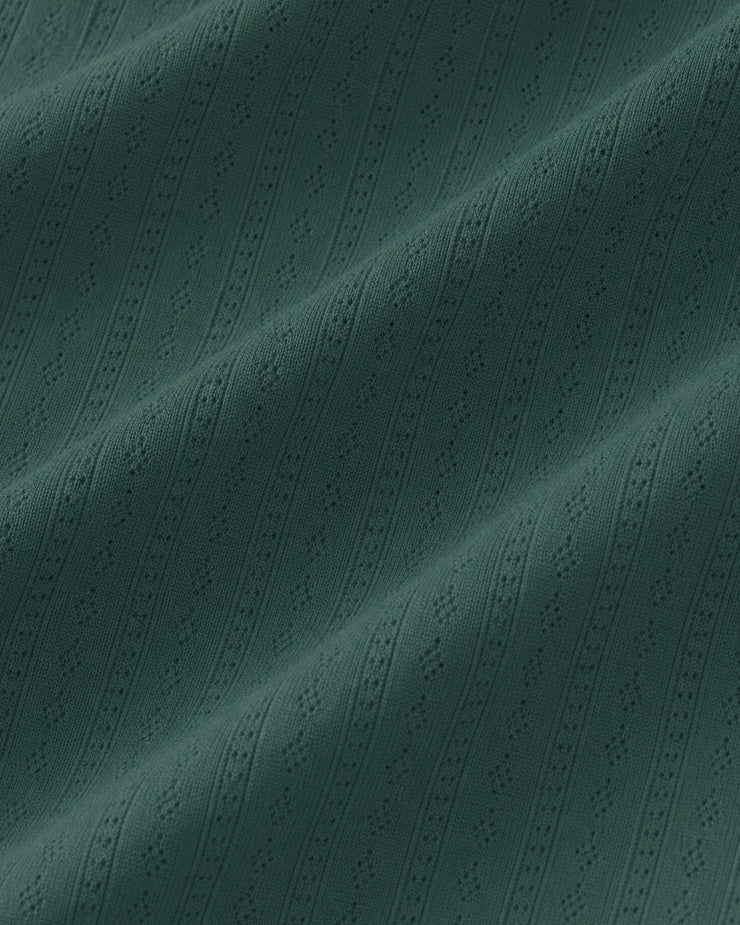 A close-up of a dark teal green fabric with a textured, vertically ribbed pattern and subtle woven details.
