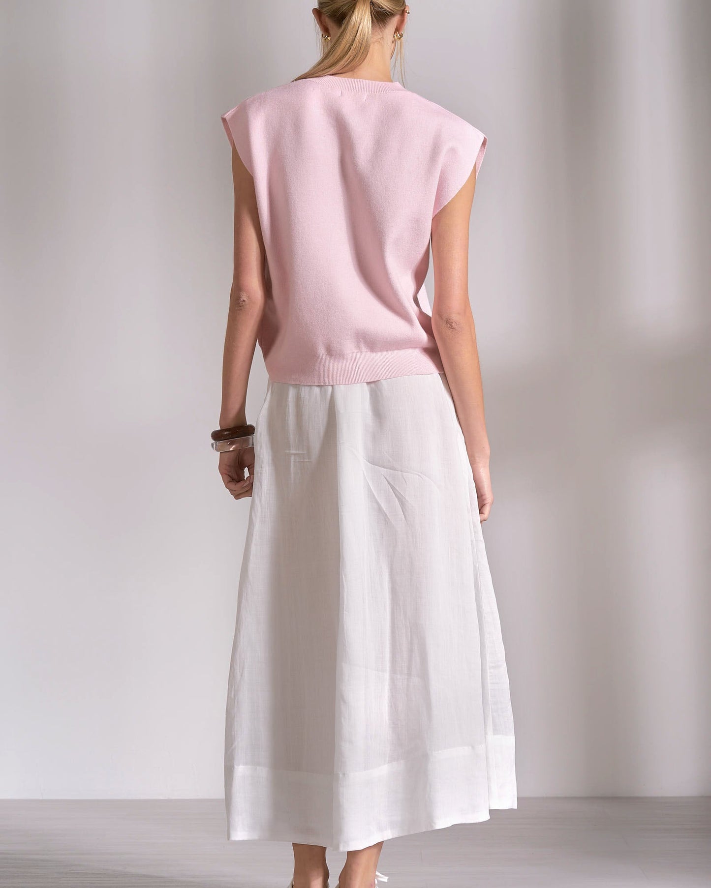Person wearing a pink sleeveless top and white pants against a plain background