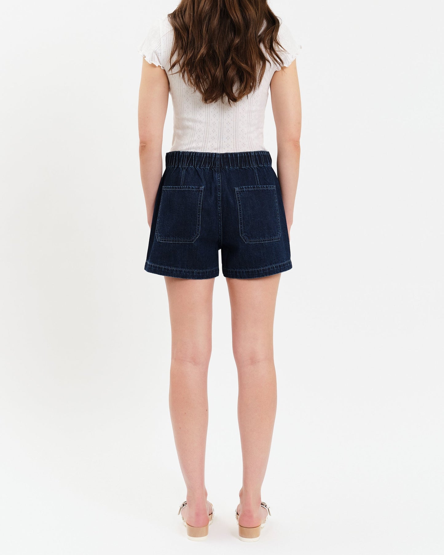 Person wearing a white top and dark denim shorts on a white background