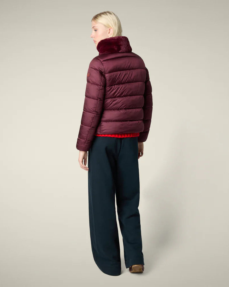 Person wearing a burgundy puffer jacket and dark pants on a plain background