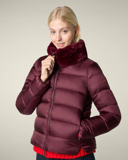 Woman wearing a maroon puffer jacket with a fur-lined hood on a beige background
