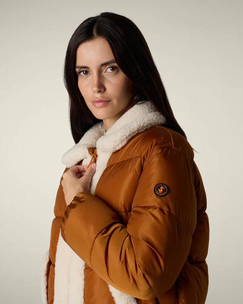 Woman wearing a brown puffer jacket with white fur lining on a neutral background