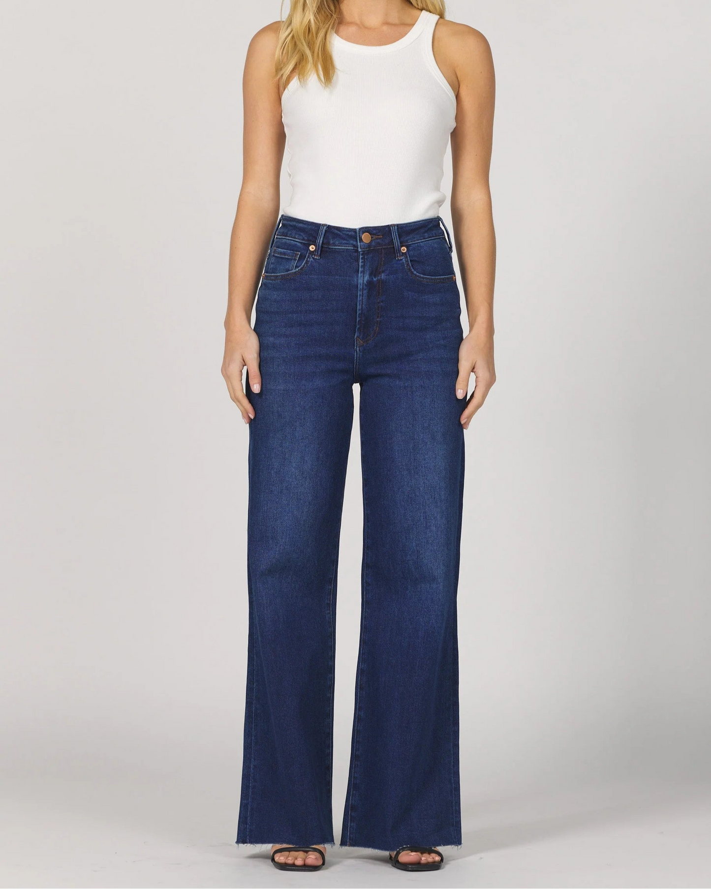 Woman wearing a white sleeveless top and blue jeans on a plain background