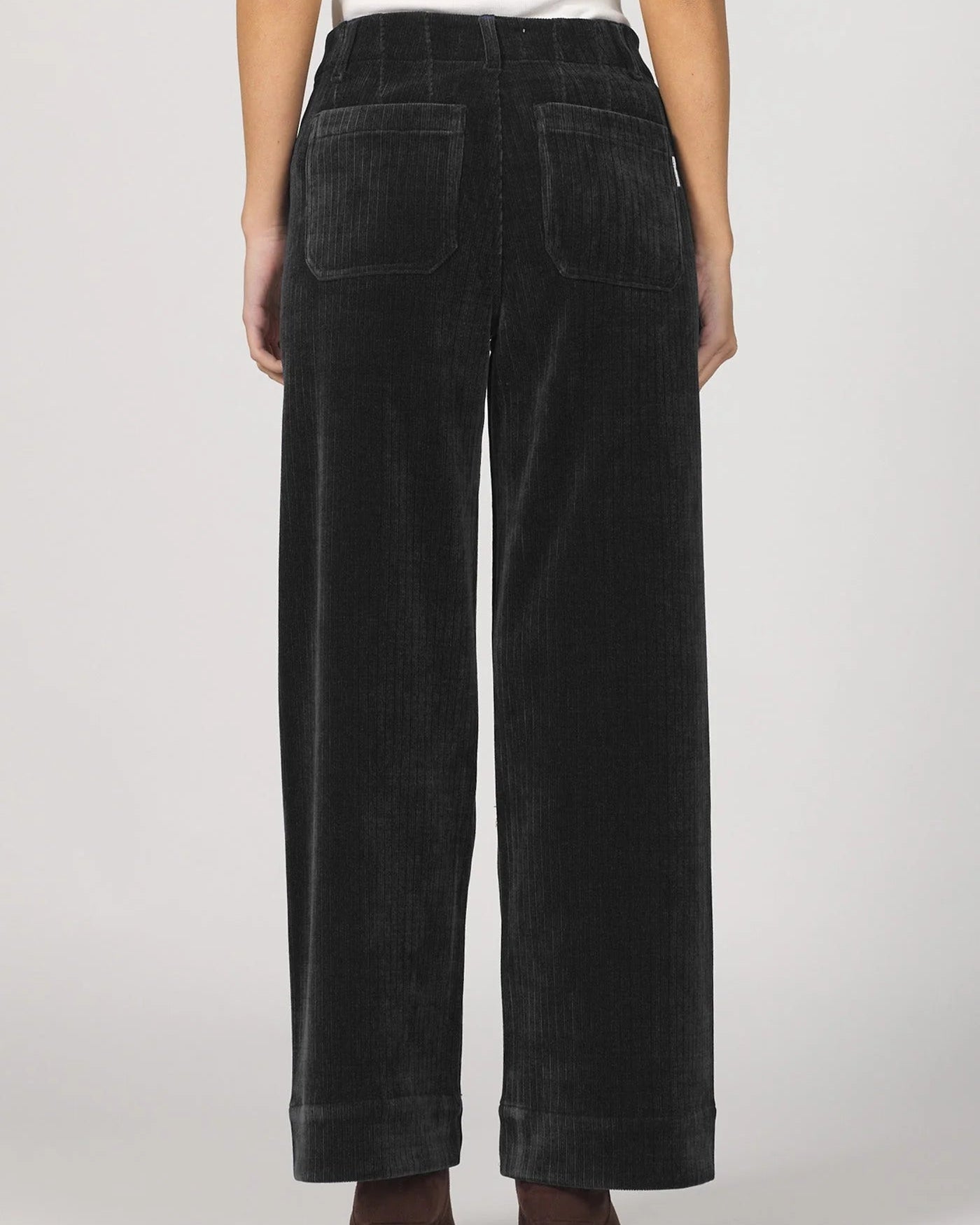 Black corduroy pants worn by a person on a white background