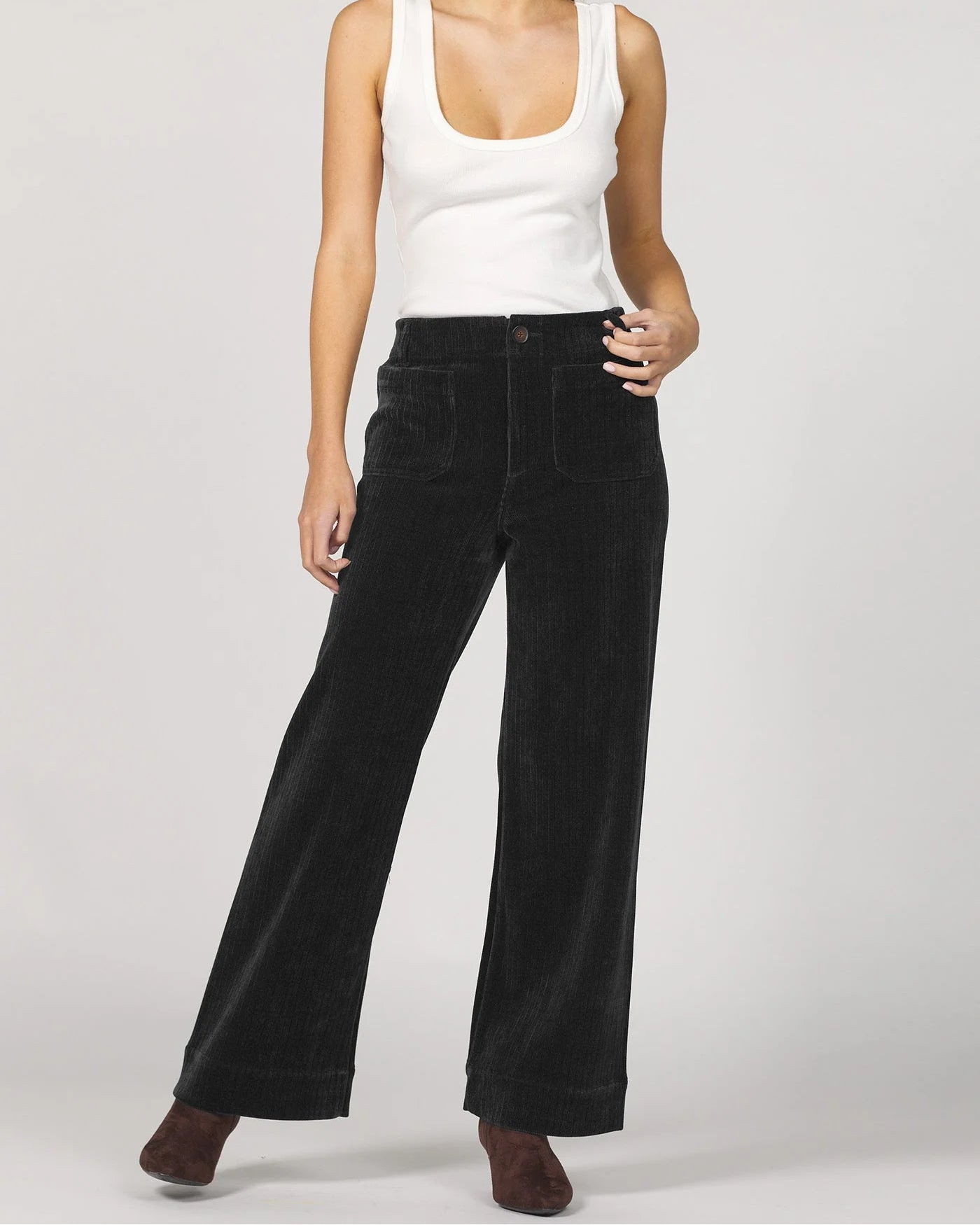 Woman wearing a white tank top and black wide-leg pants on a plain background