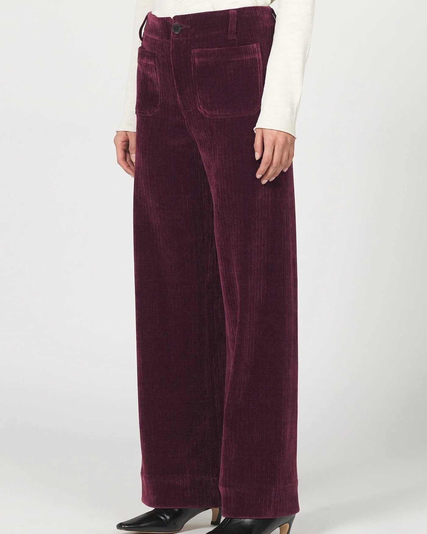 Burgundy corduroy pants worn by a person on a white background