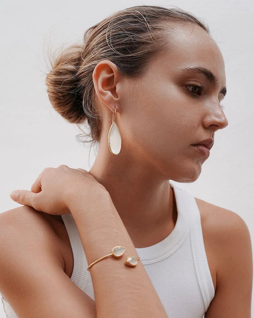 Woman wearing gold earrings and bracelet against a neutral background
