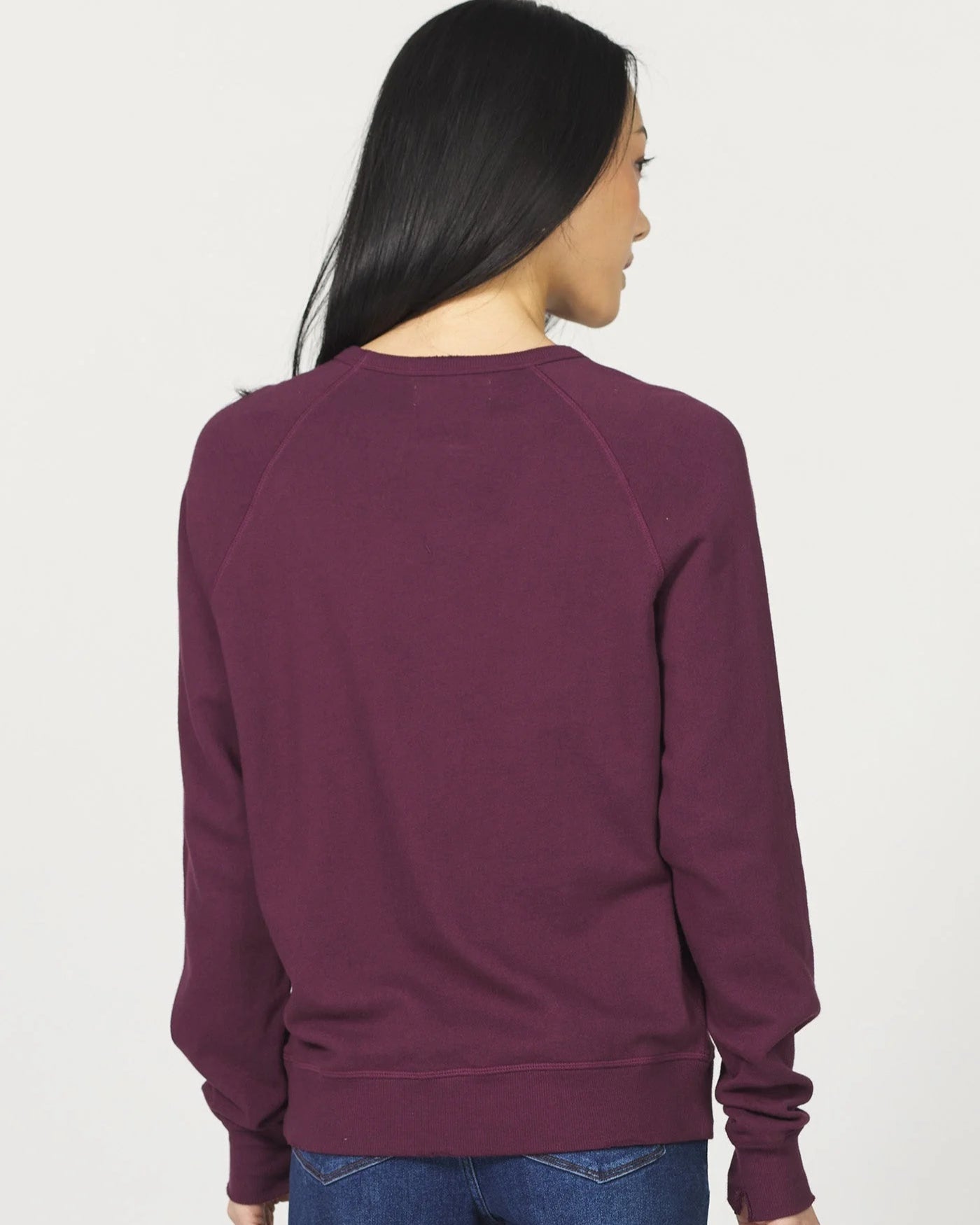 Person wearing a maroon sweatshirt and blue jeans on a white background