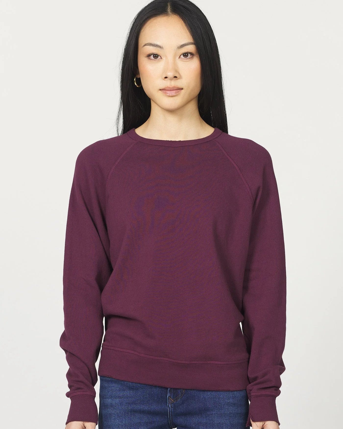 Person wearing a maroon sweater and blue jeans on a white background