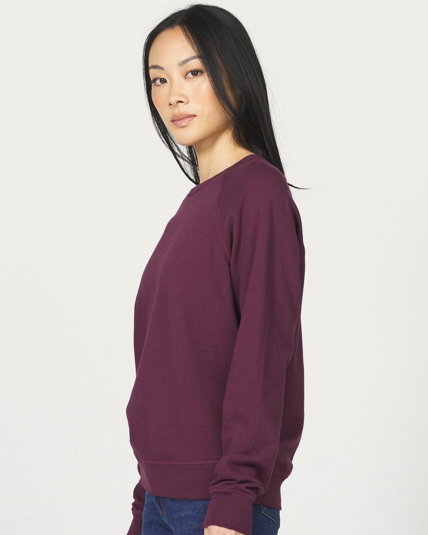 Woman wearing a maroon sweater and blue jeans on a white background