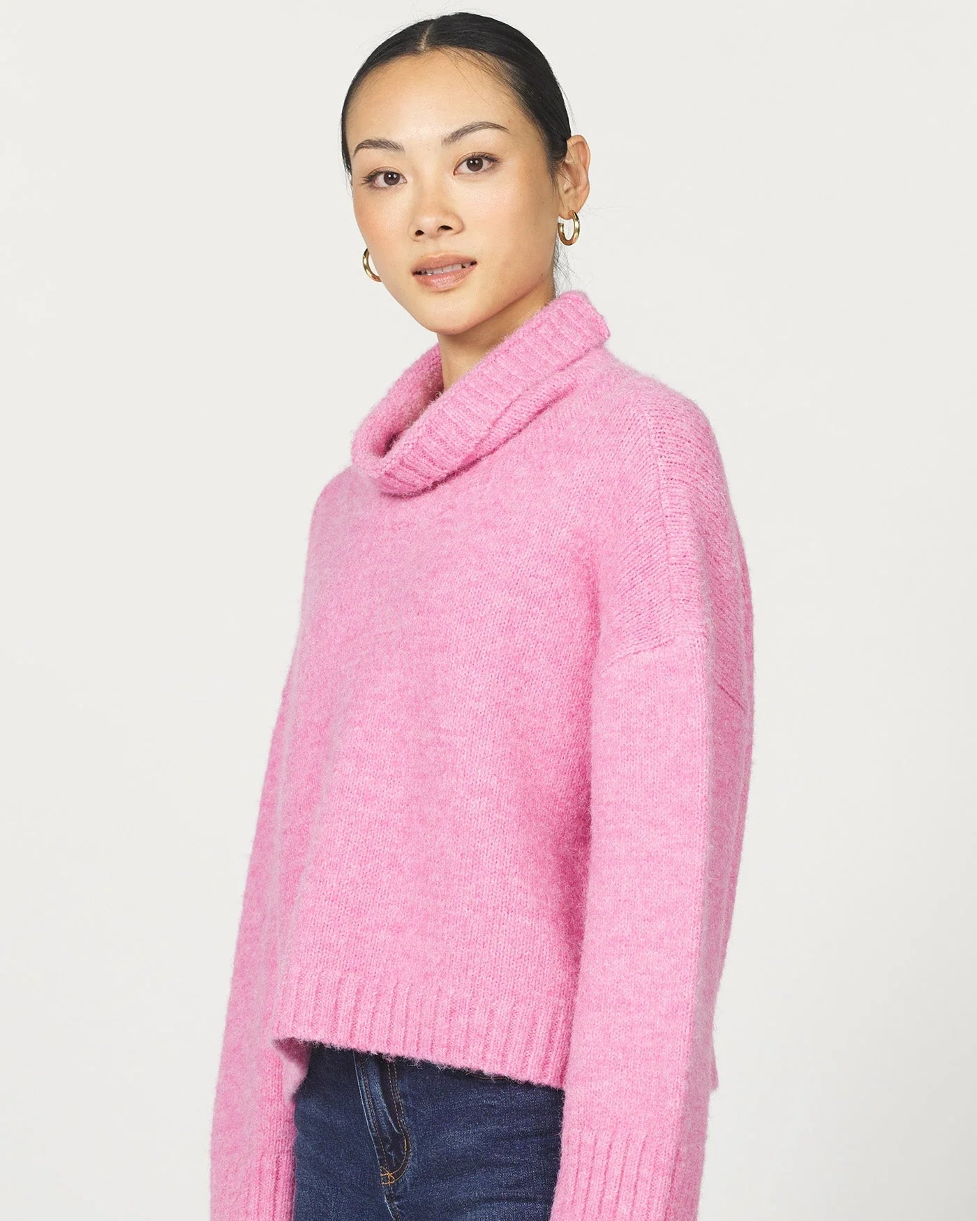 Person wearing a pink sweater with a cowl neck on a white background