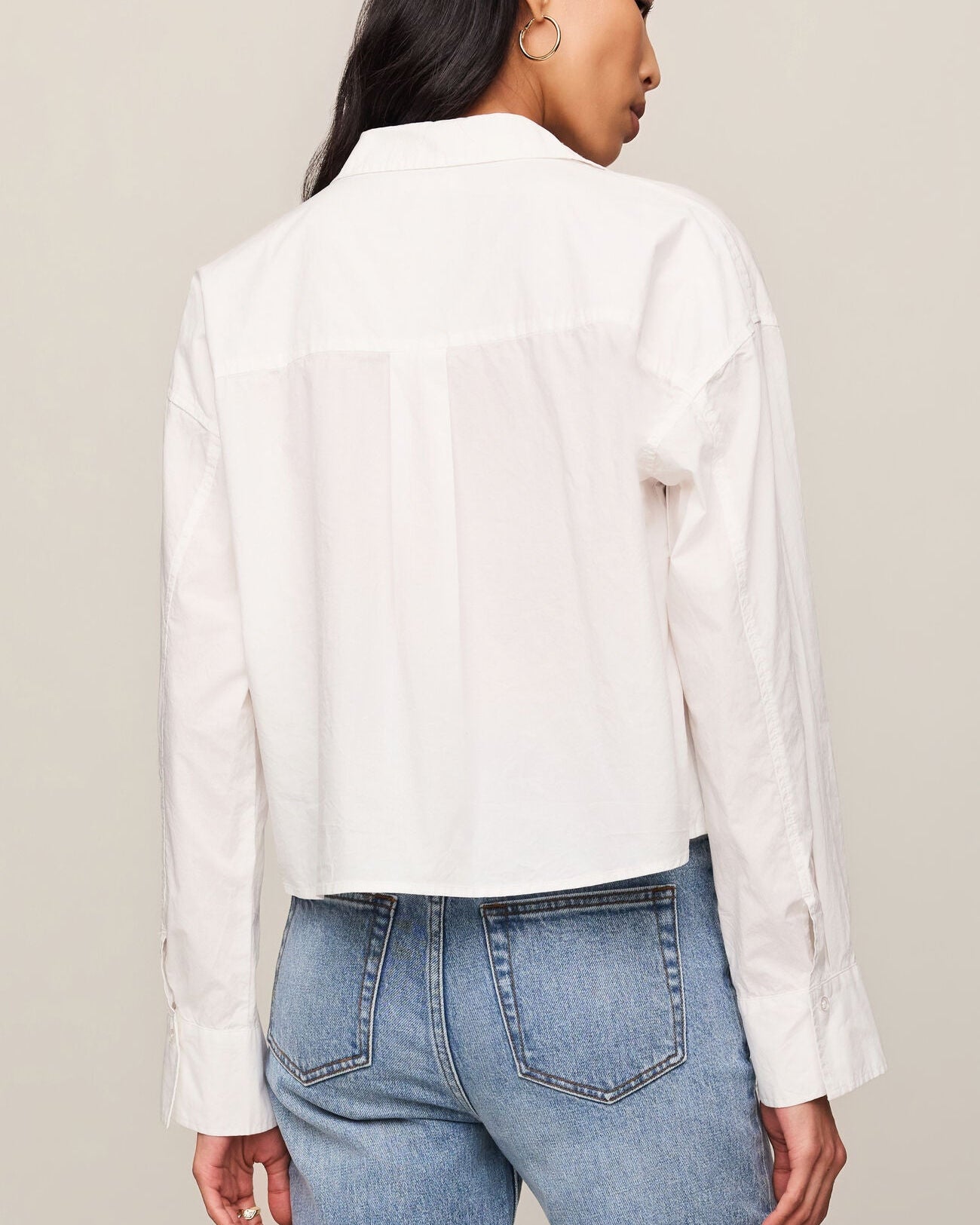 Person wearing a white shirt and blue jeans against a neutral background
