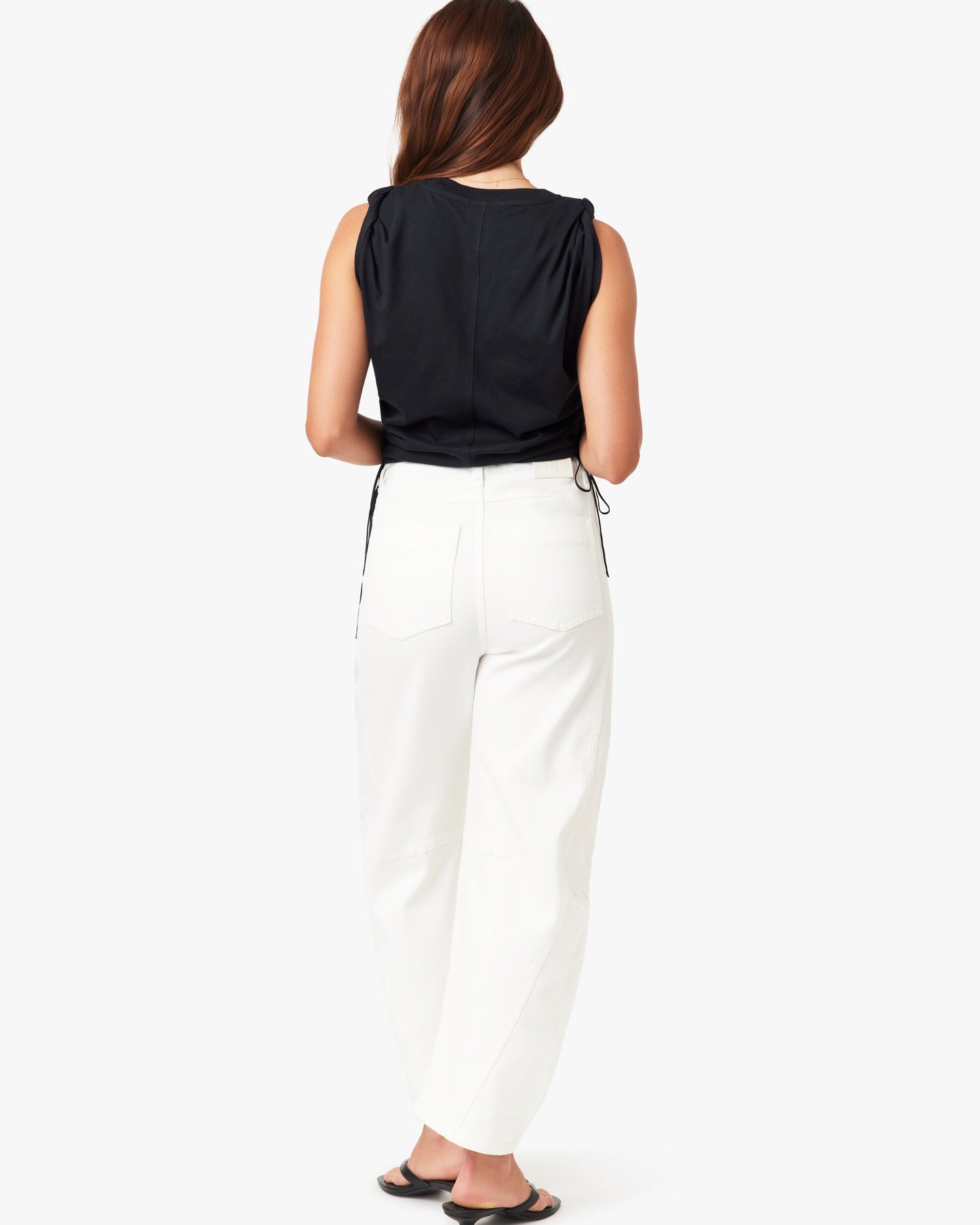 Woman wearing a black sleeveless top and white pants on a white background