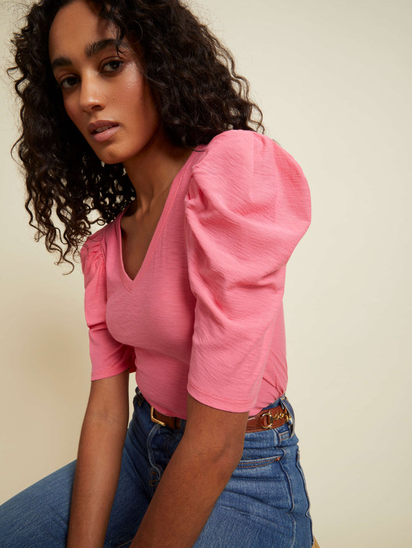 Model wearing Nation LTD Jillian Bold Shoulder V Neck in party pink color wearing jeans and brown belt on a off white background