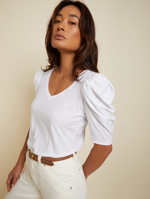 Model wearing Nation LTD Jillian Bold Shoulder V Neck top wearing white pants and brown belt on a off white background