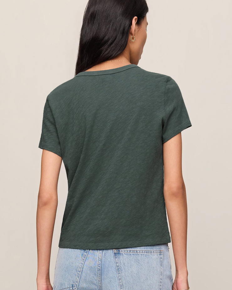 Person wearing a green t-shirt and light blue jeans on a beige background