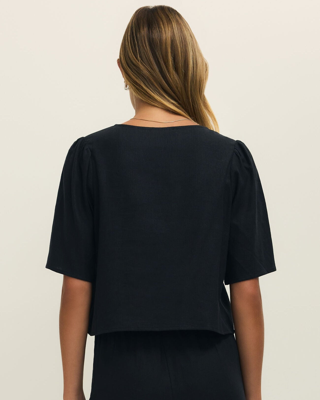 Person wearing a black top and pants on a beige background