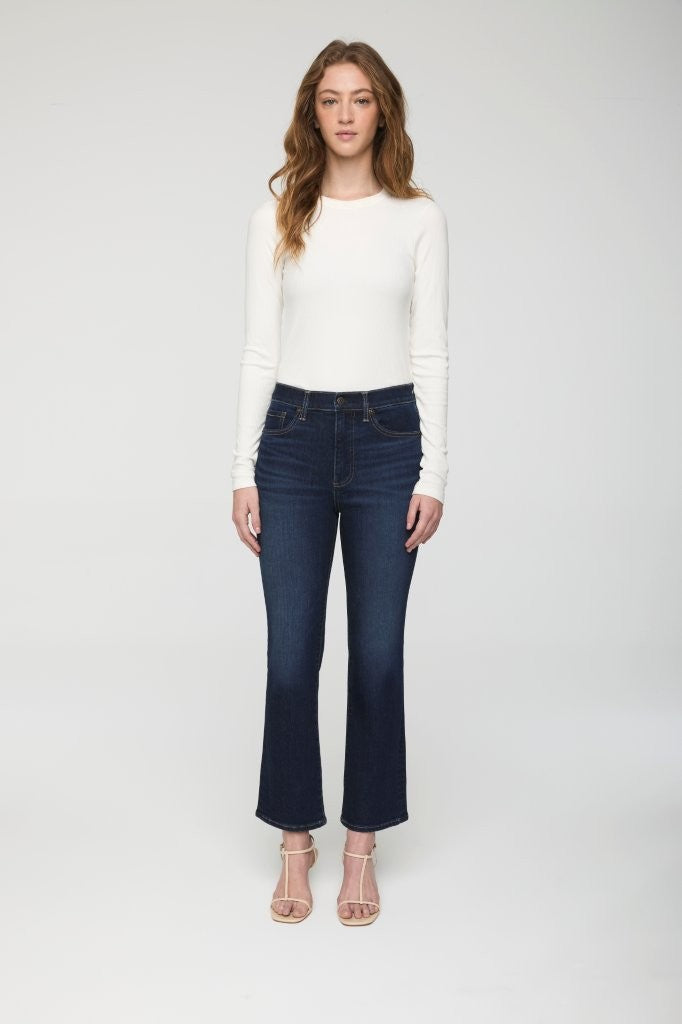 Woman wearing a white long-sleeve top and dark blue jeans on a white background