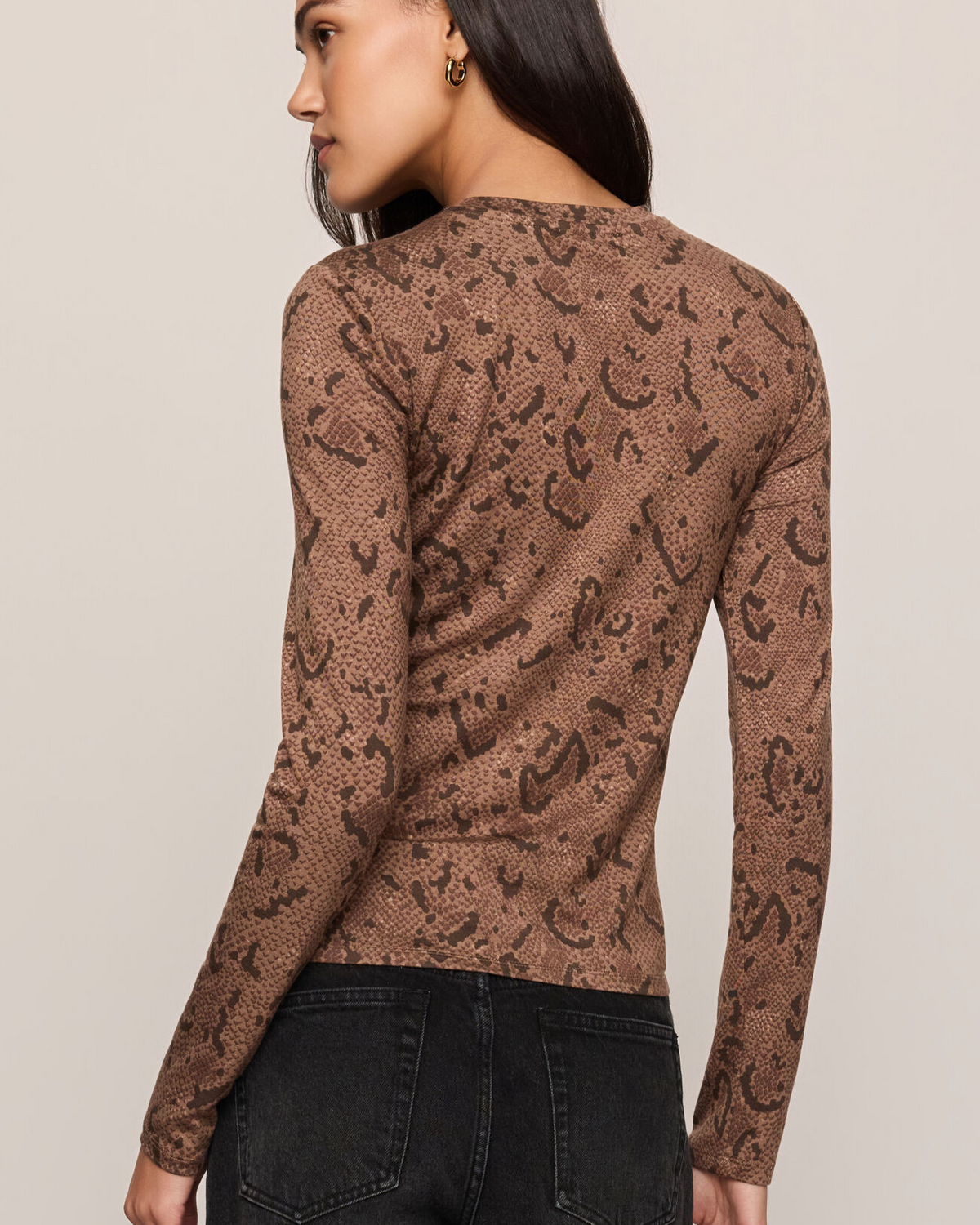 A woman shown from the back wearing a brown long-sleeve knit top with a dark brown leopard print pattern, paired with black jeans, against a solid light beige background.