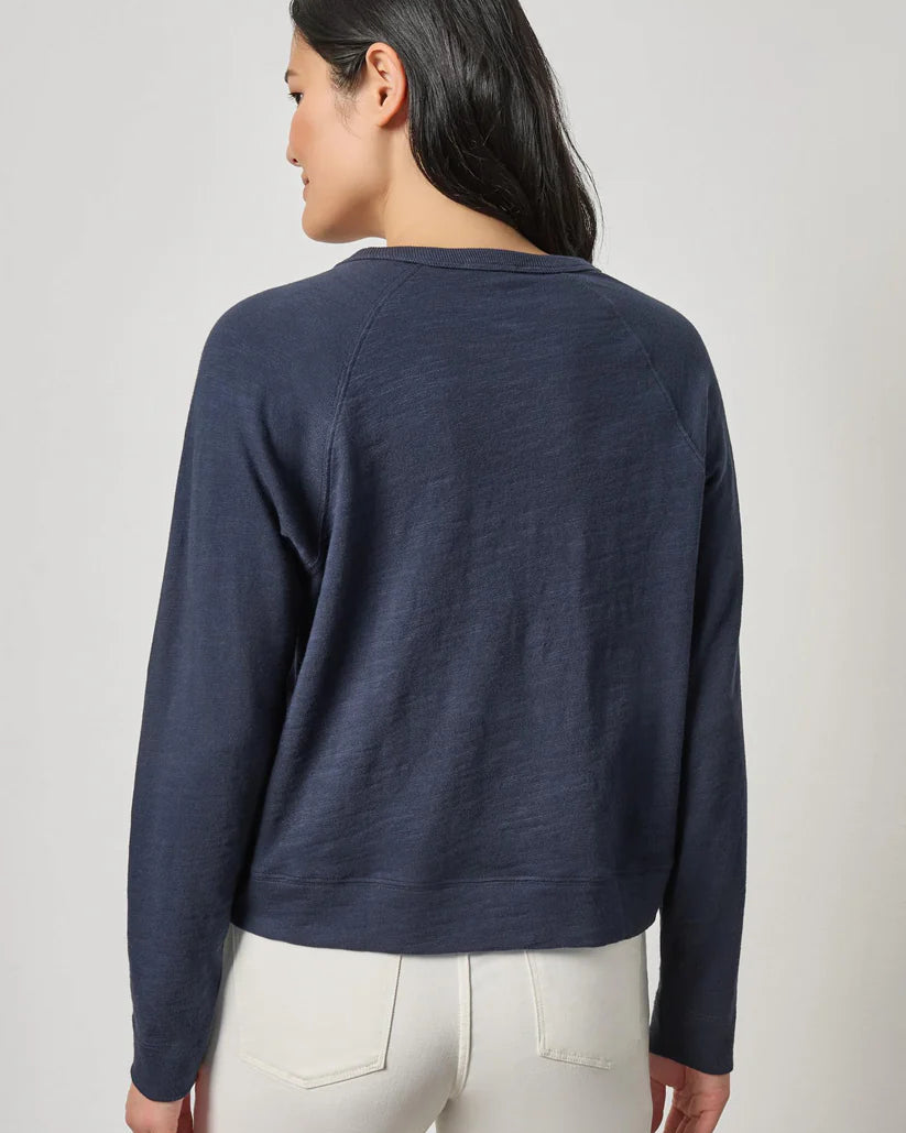 Woman wearing a navy long-sleeve shirt and white pants on a light gray background