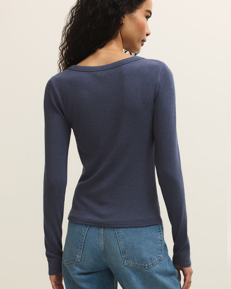Woman wearing a navy long-sleeve top and blue jeans on a beige background