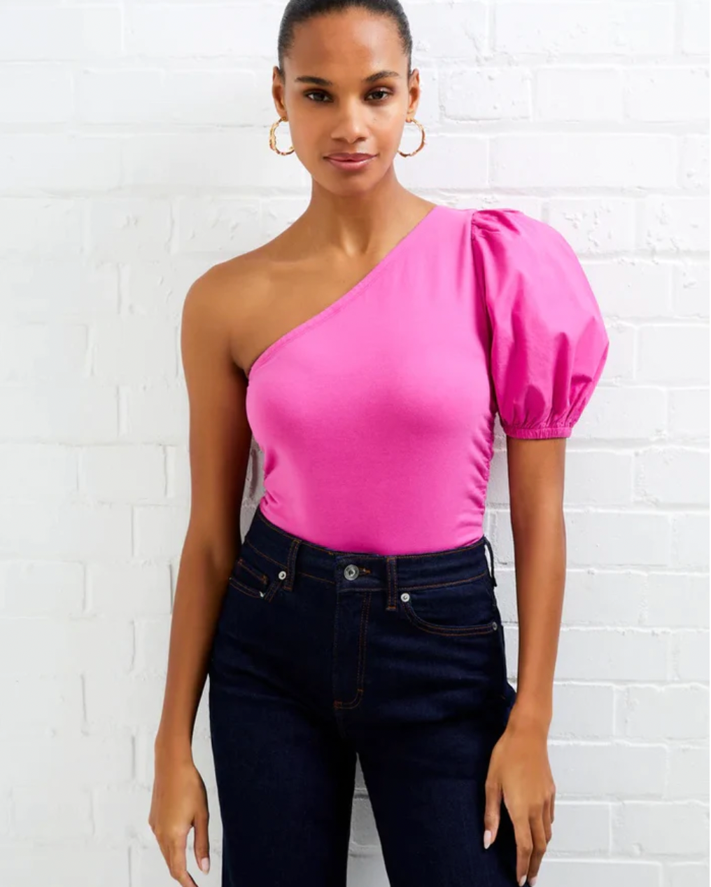 Model wearing French Connection Rosanna Cot Mix 1 Shoulder Top in wild rosa wearing jeans on a white brick background