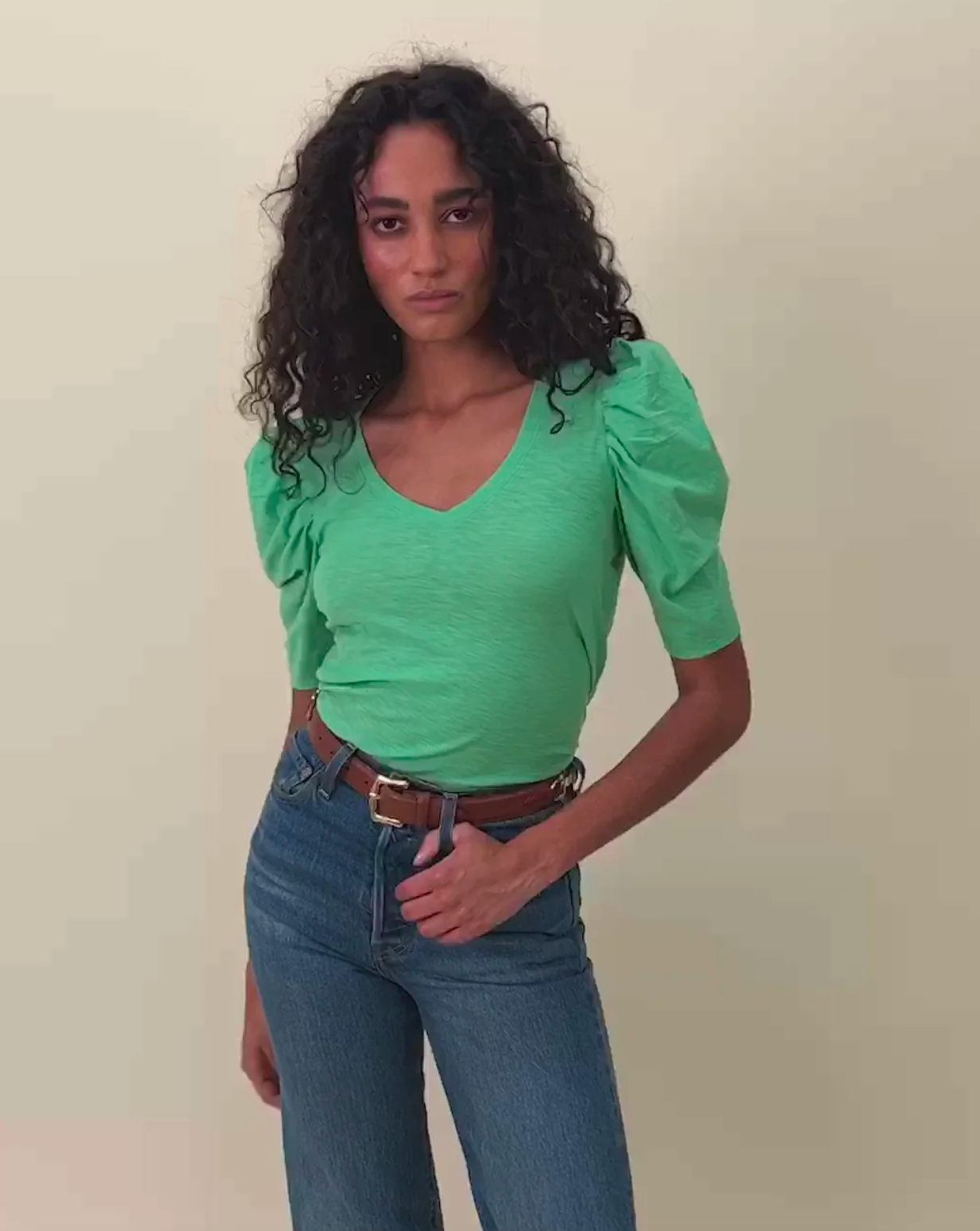 Model Wearing Nation LTD Jillian Bold Shoulder V Neck Granny Color wearing Jeans and a brown belt on a beige background