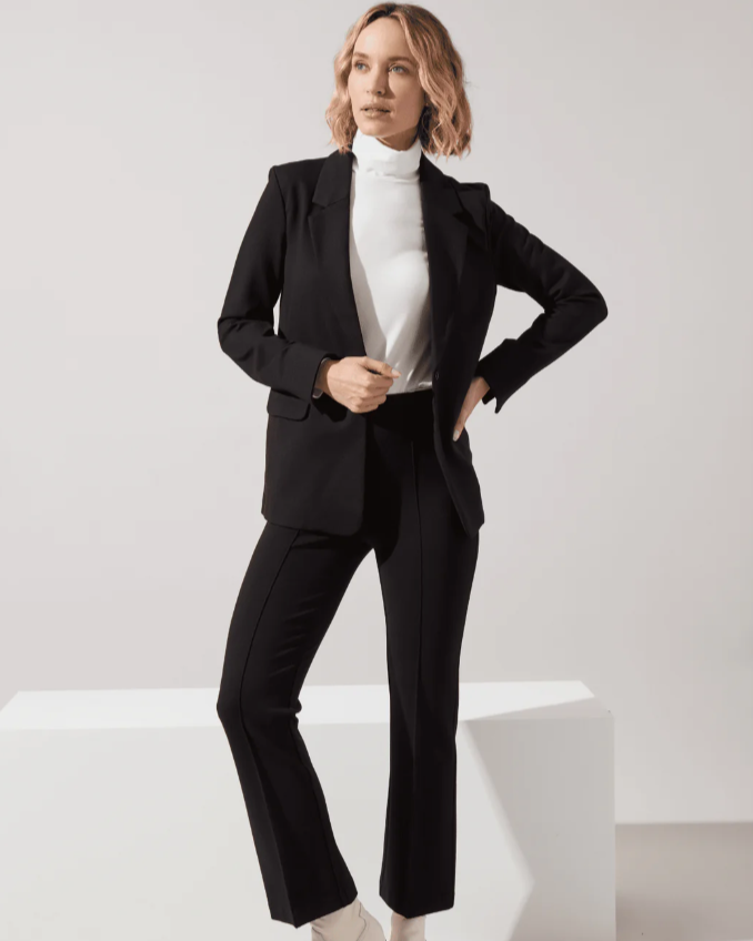 Woman wearing a black suit with a white top and white shoes on a light background