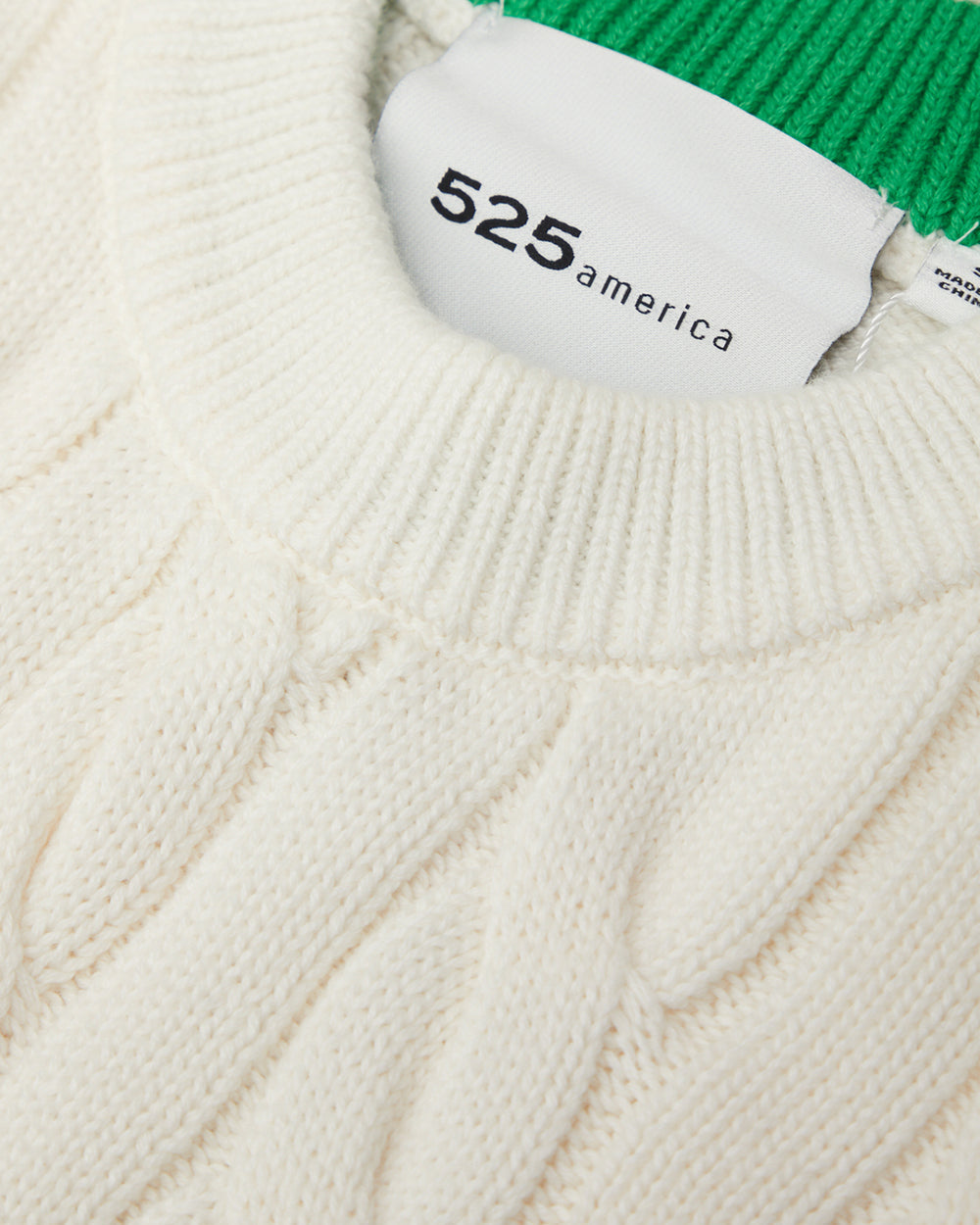 Close-up of a cable-knit sweater with a brand label on a white background